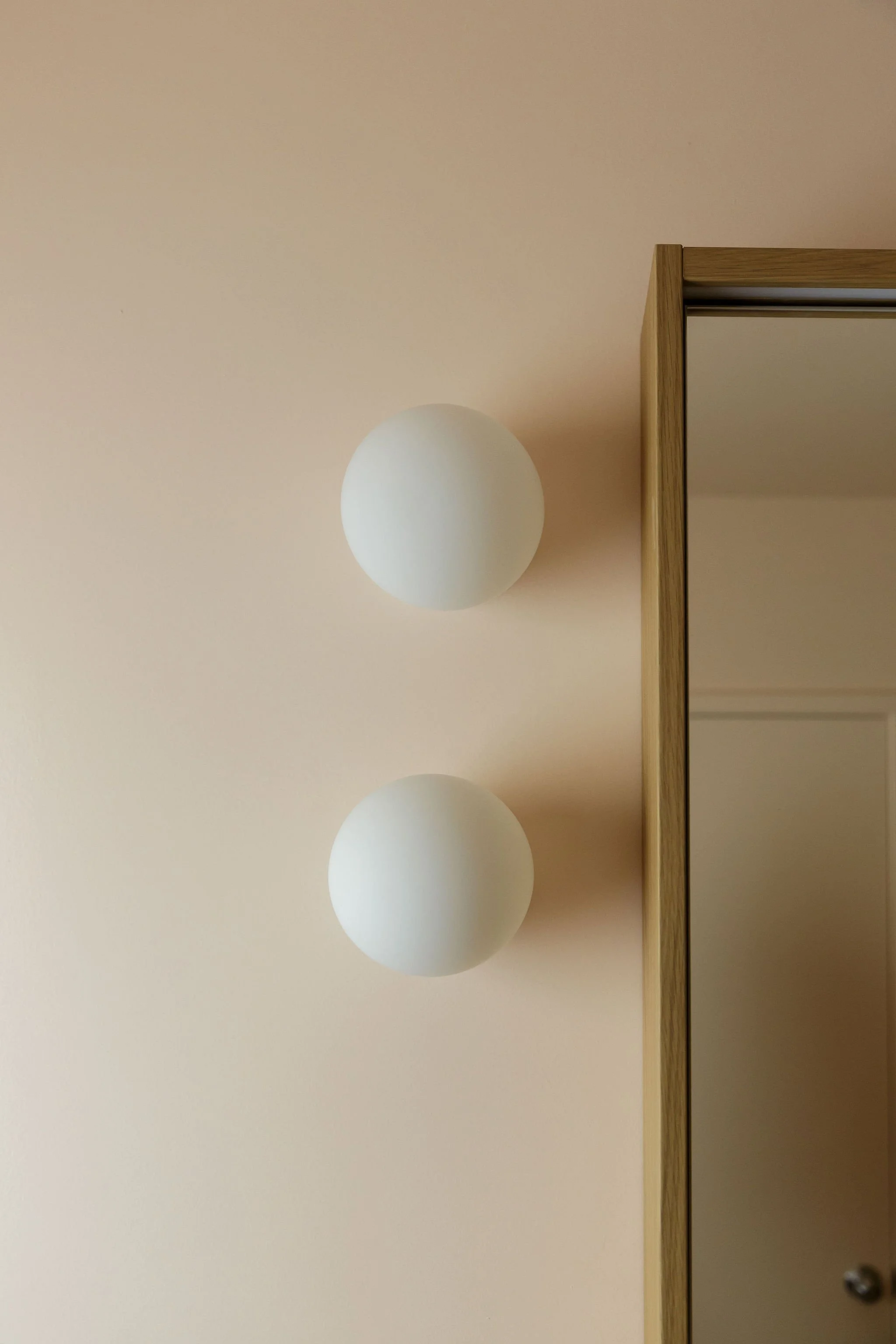 Interior wall with two round, white, light fixtures and a wooden-framed cabinet on the right side.