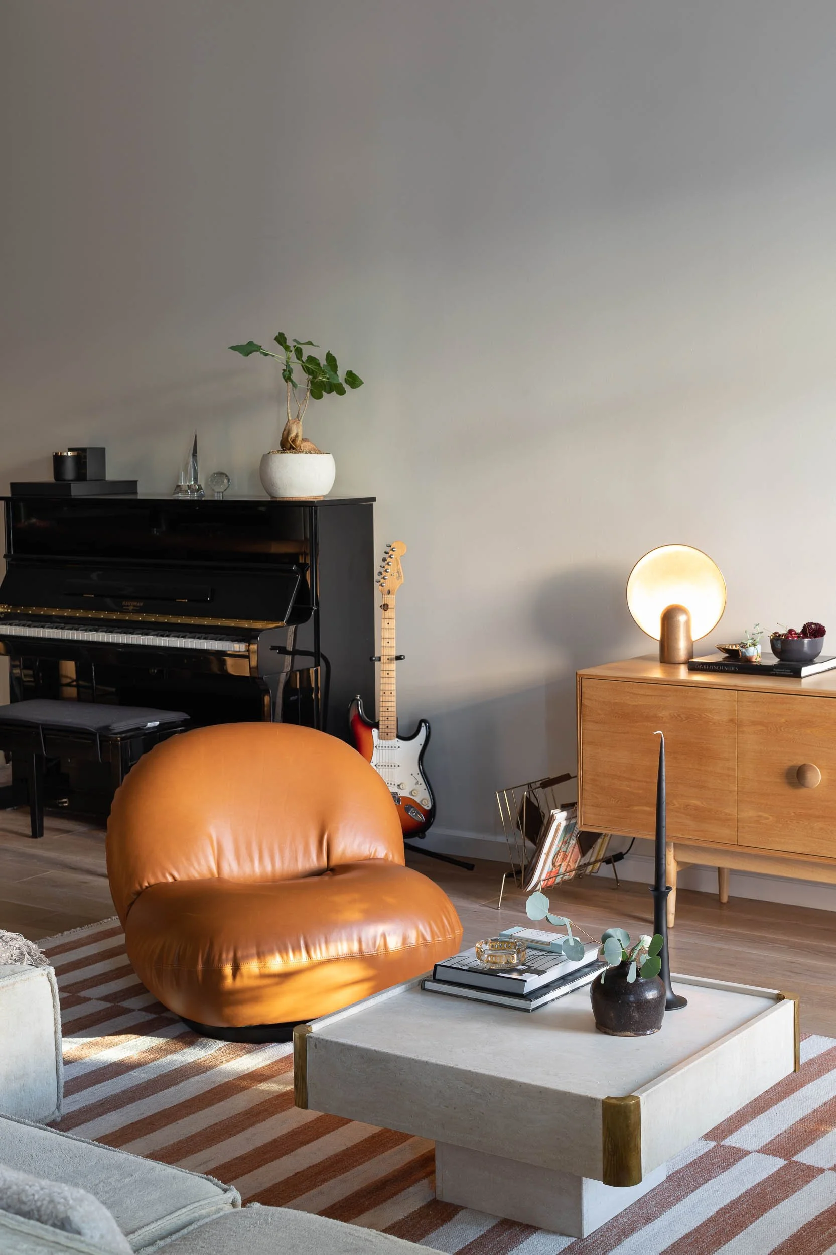 Living room with black piano, electric guitar, tan leather chair, coffee table with decor, and wooden sideboard with lamp