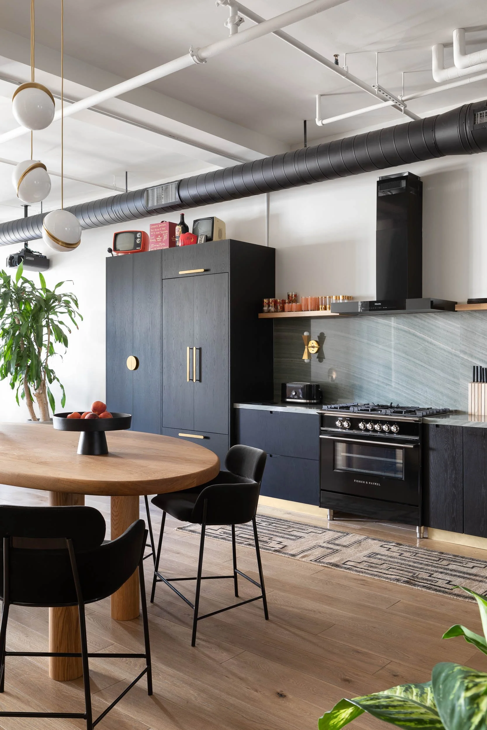 Modern black kitchen with dining table, black chairs, black cabinets, gas stove, and outdoor plants.