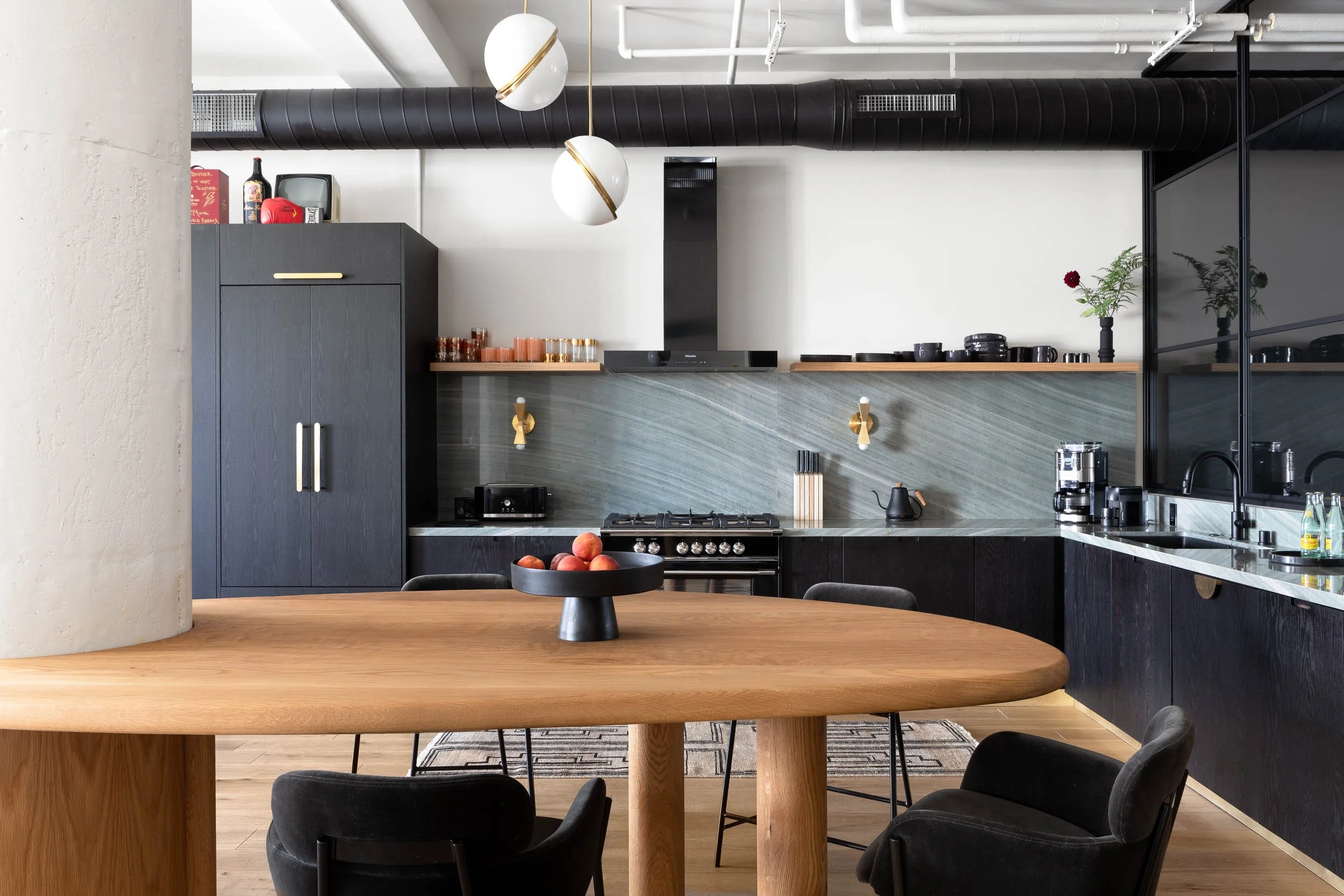 Modern kitchen with black cabinets, a wooden dining table, black chairs, and decorative lighting fixtures.