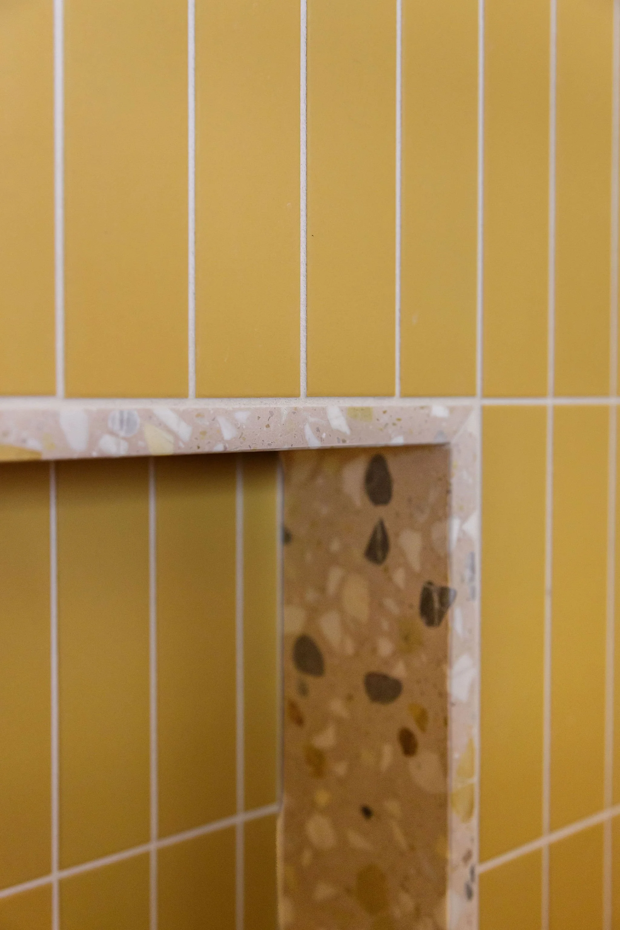 Close-up of yellow and pink tiled surfaces with grout lines and a corner of a tiled wall.