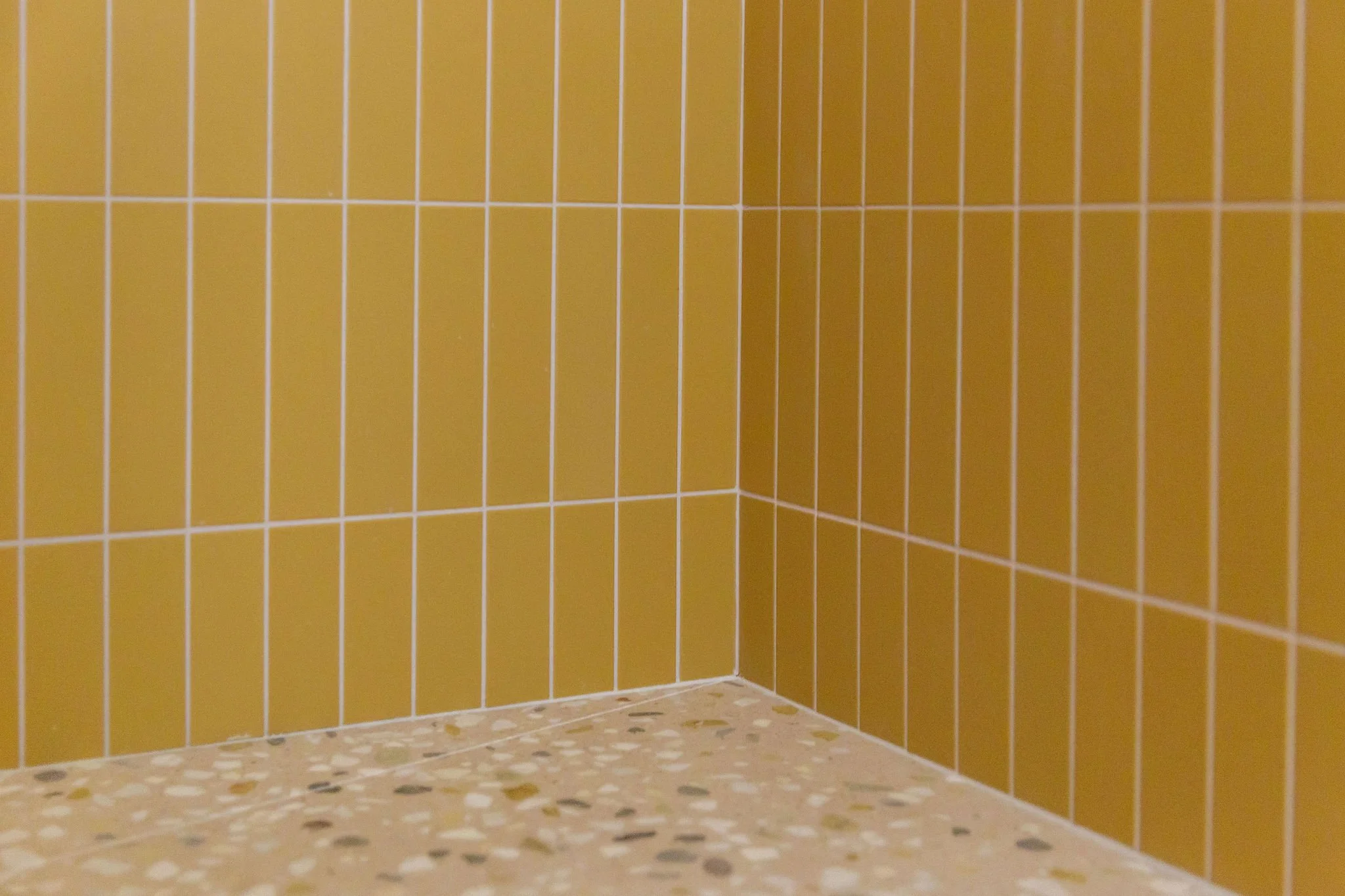 View of a corner of a tiled bathroom with yellow and pink terrazzo tiles.