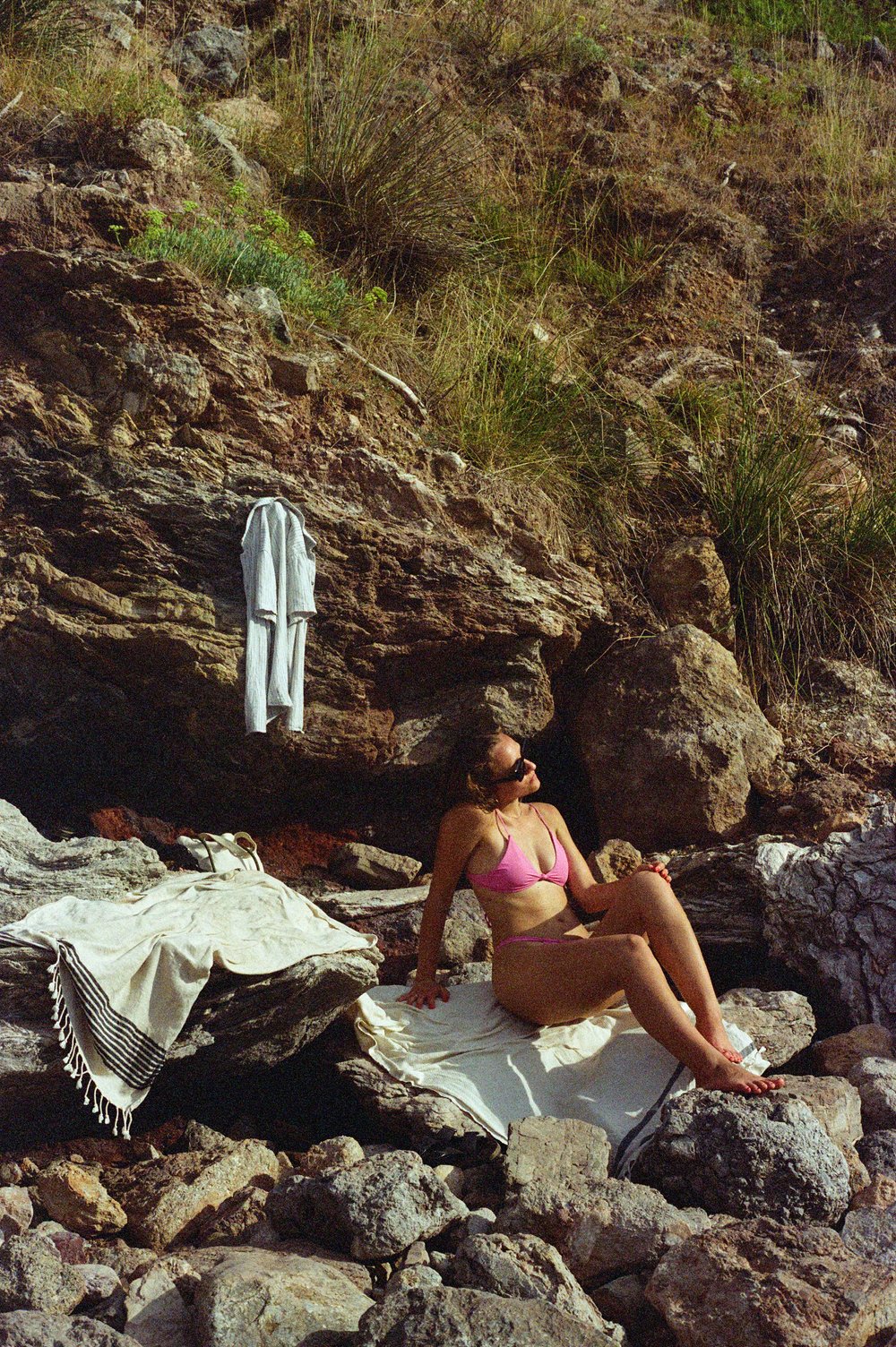  woman laying on rocky beach with towel hanging from rock above on Mallorca, Spain 