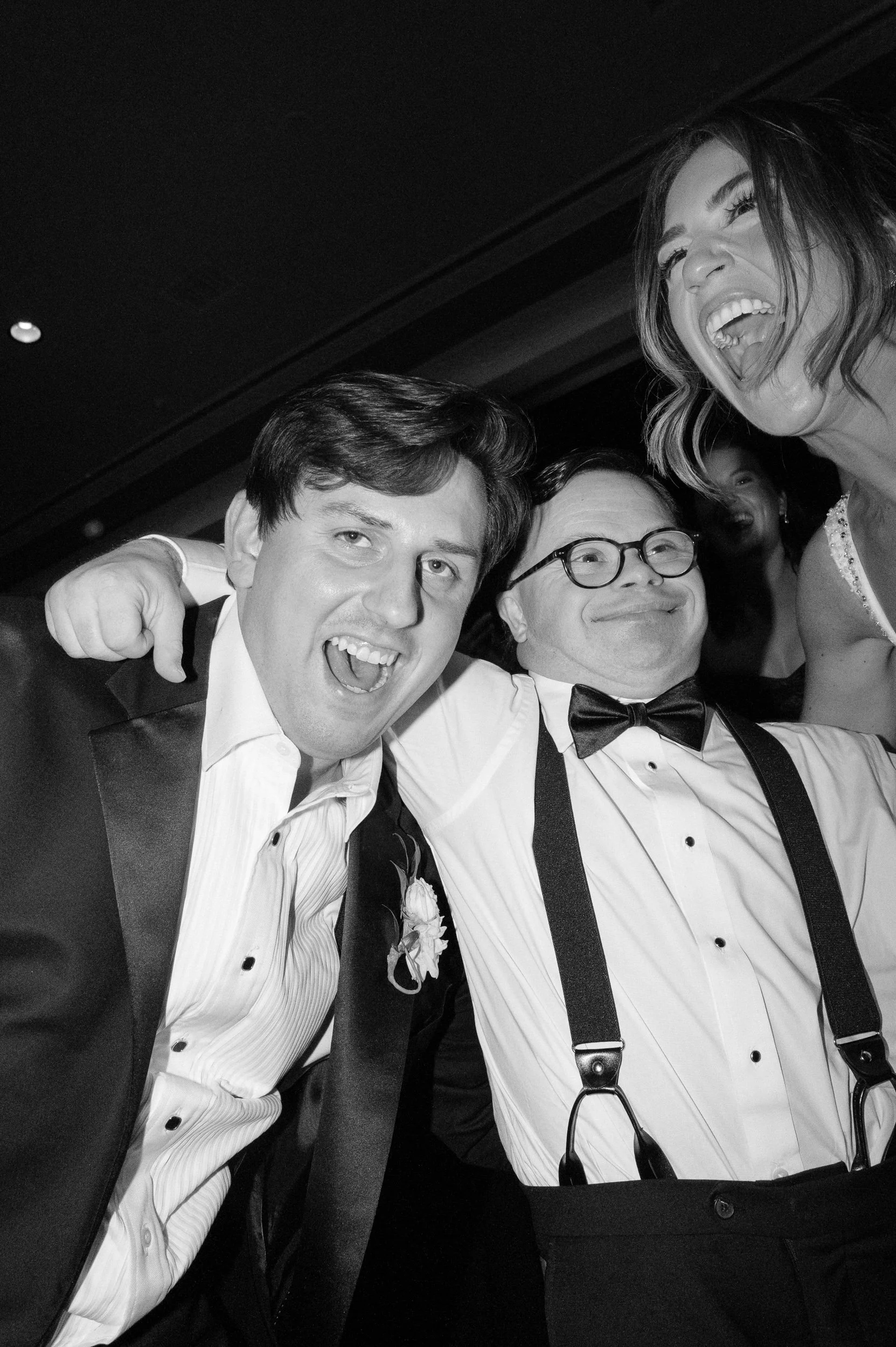 Three people at a celebration or party smiling and having fun. Two men and a woman, dressed in formal attire.