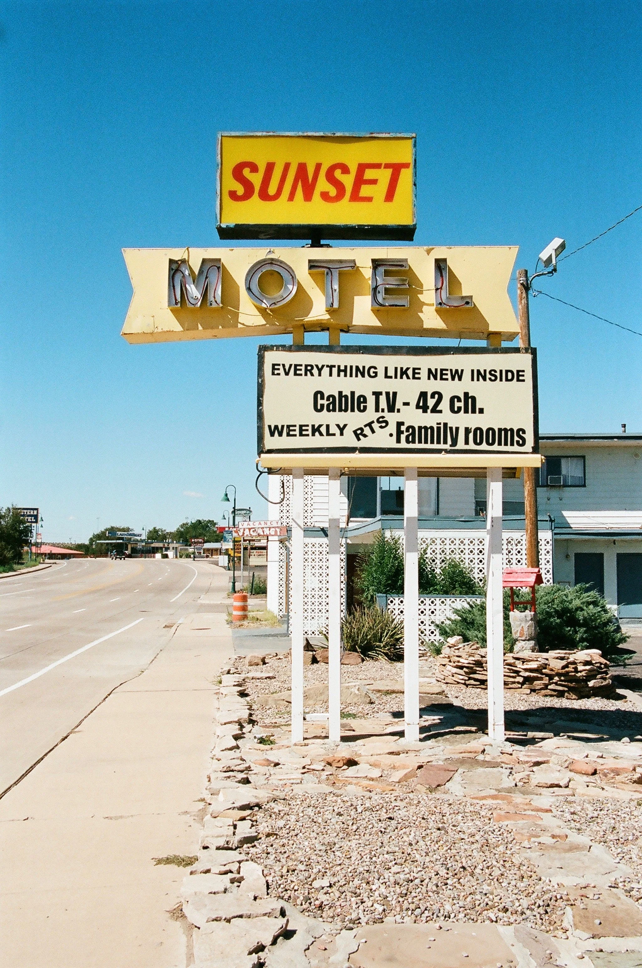 A vintage roadside motel sign for Sunset Motel with neon lights, advertising cable TV, weekly rates, and family rooms, under a clear blue sky.