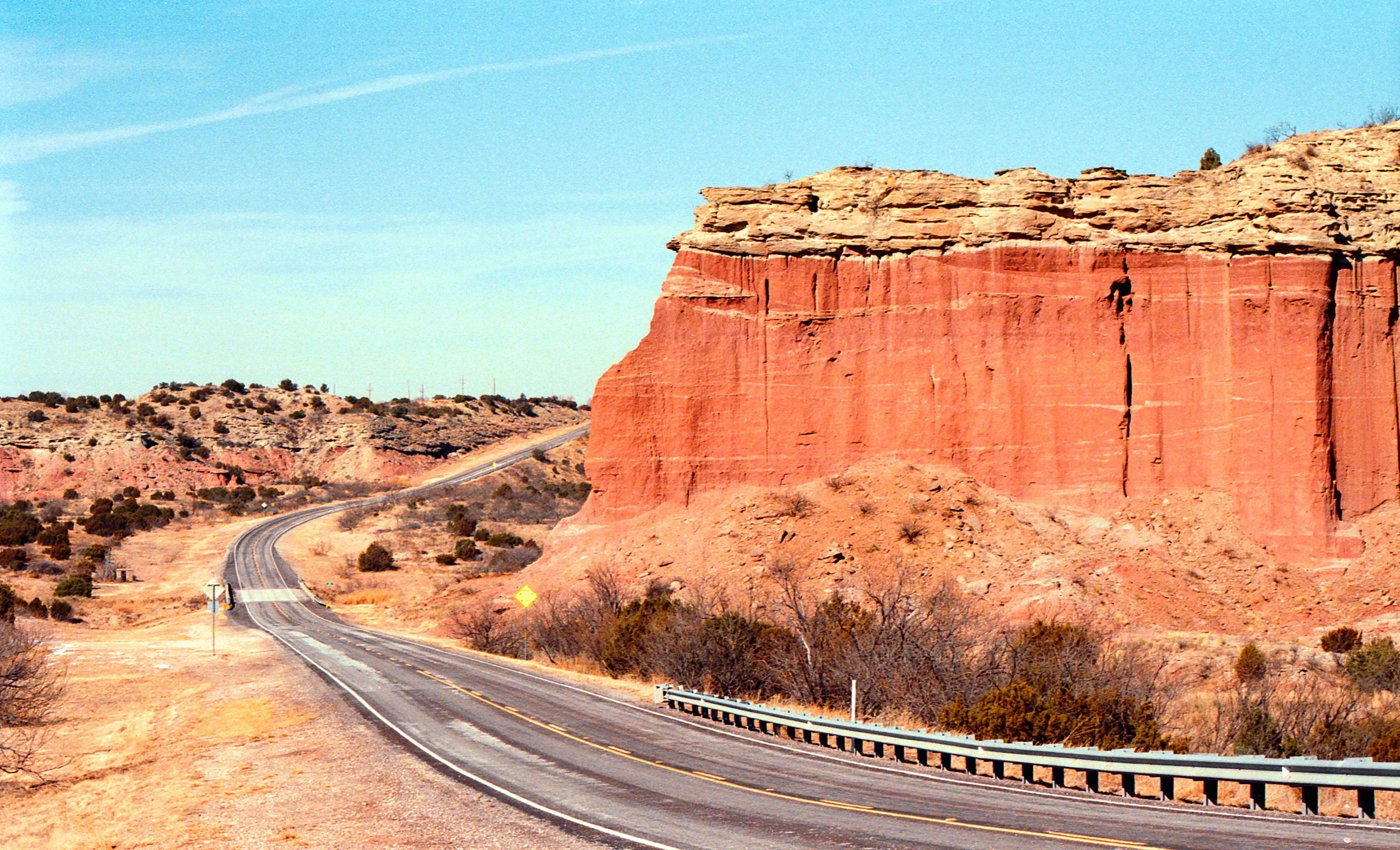 A winding road through a desert landscape with red rock formations and sparse vegetation under a clear blue sky.