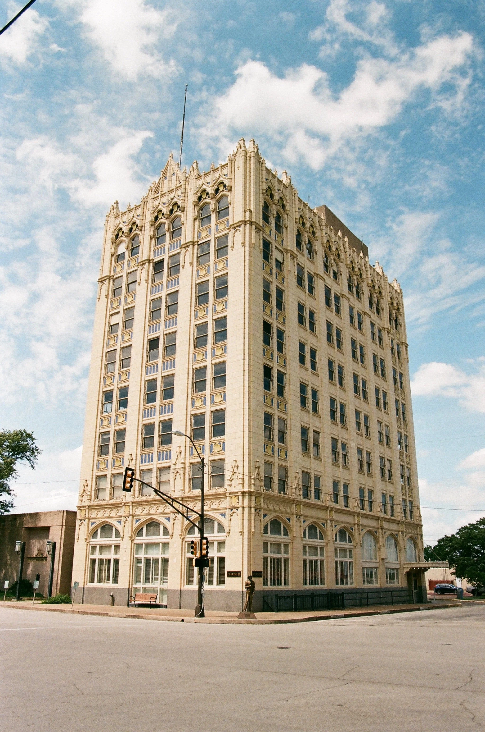 A tall historic building with ornate architectural details on a city street corner, under a partly cloudy sky.