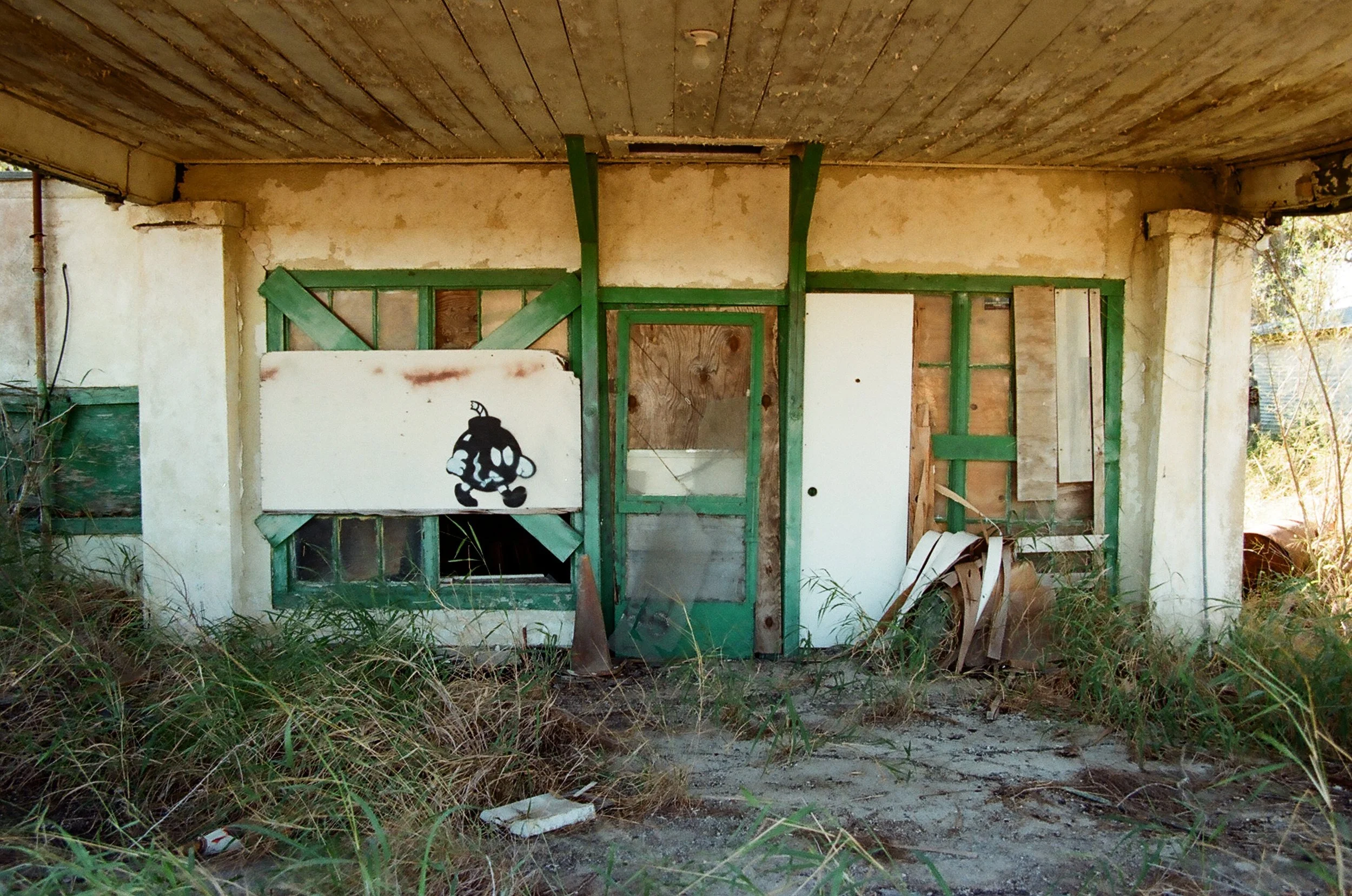 Abandoned building with damaged walls, overgrown weeds, and graffiti of a cartoon character on the front panel.