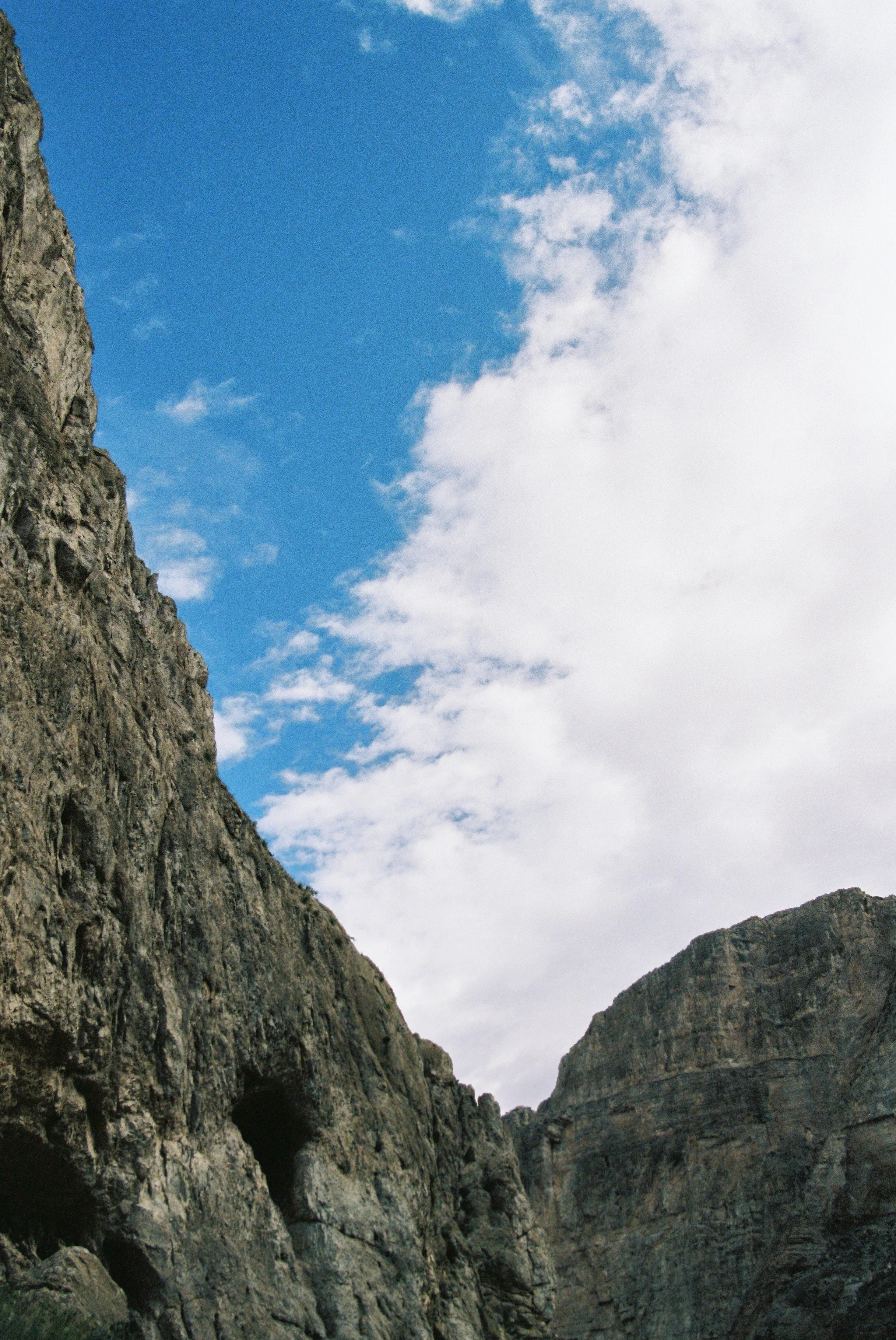 View of rocky mountain cliffs with blue sky and clouds above.