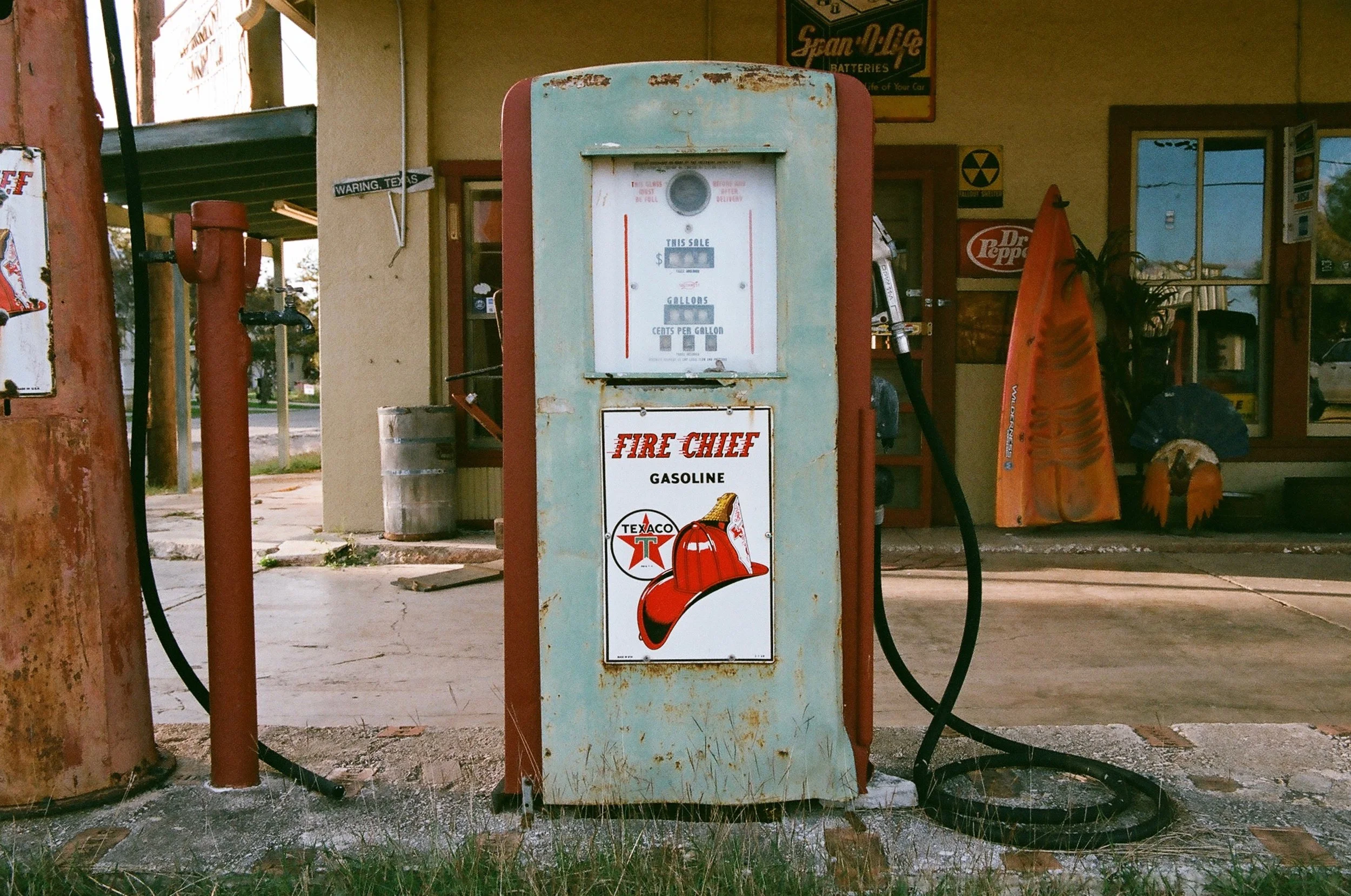Vintage F Day Chief gasoline pump with a Texaco logo, outside an old-fashioned store or gas station with vintage signage, tools, and decor in the background.