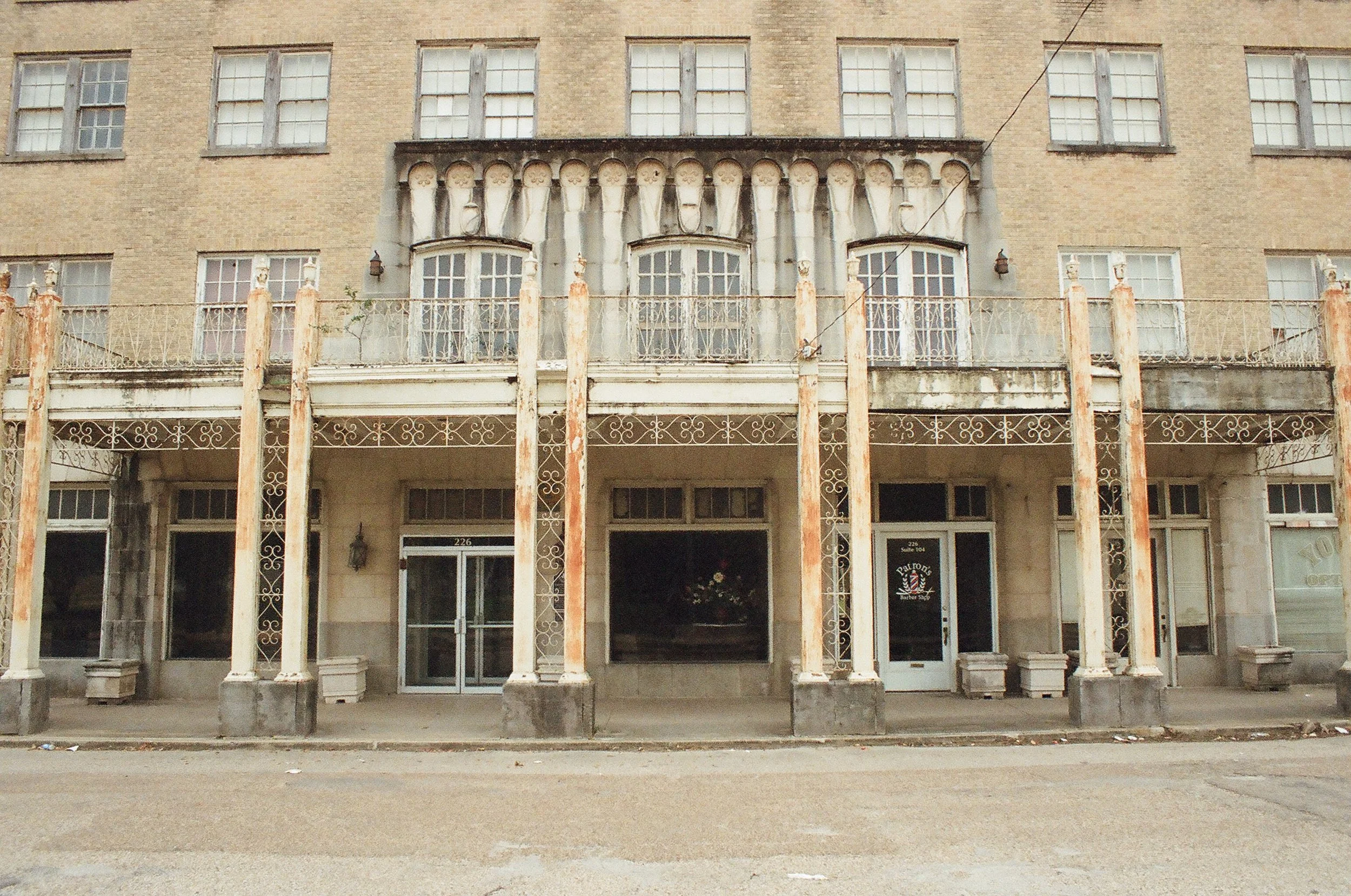 Old, abandoned building with rusted metal columns and ornate railing, featuring a barbershop on the ground floor.