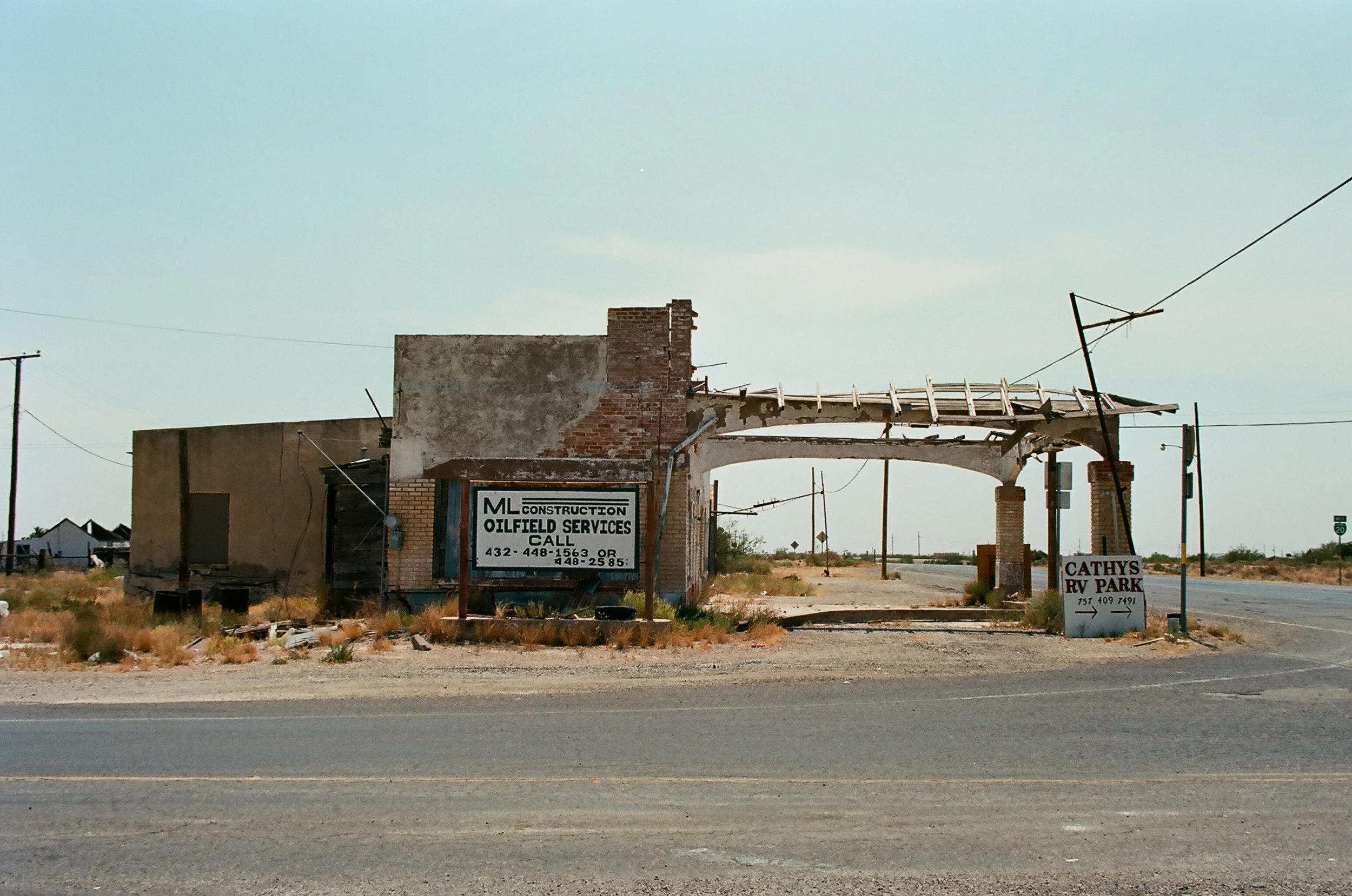 Abandoned and dilapidated building in a desert landscape, with signs for construction and RV park, under a pale blue sky.