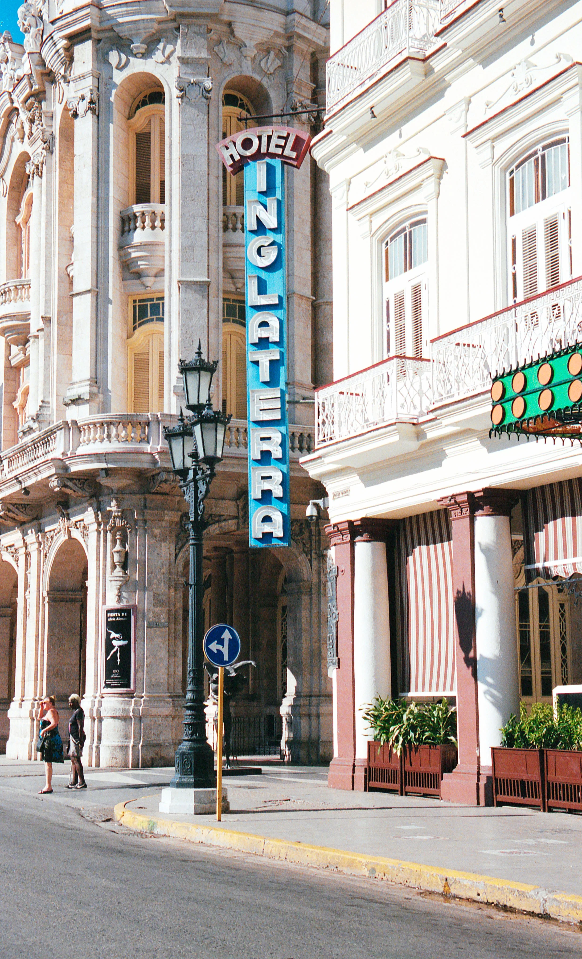 Street view of a historic hotel with a large vertical neon sign reading 'Hotel Inglarad'. The building has ornate architectural details and balconies, with a streetlamp and pedestrians in front.