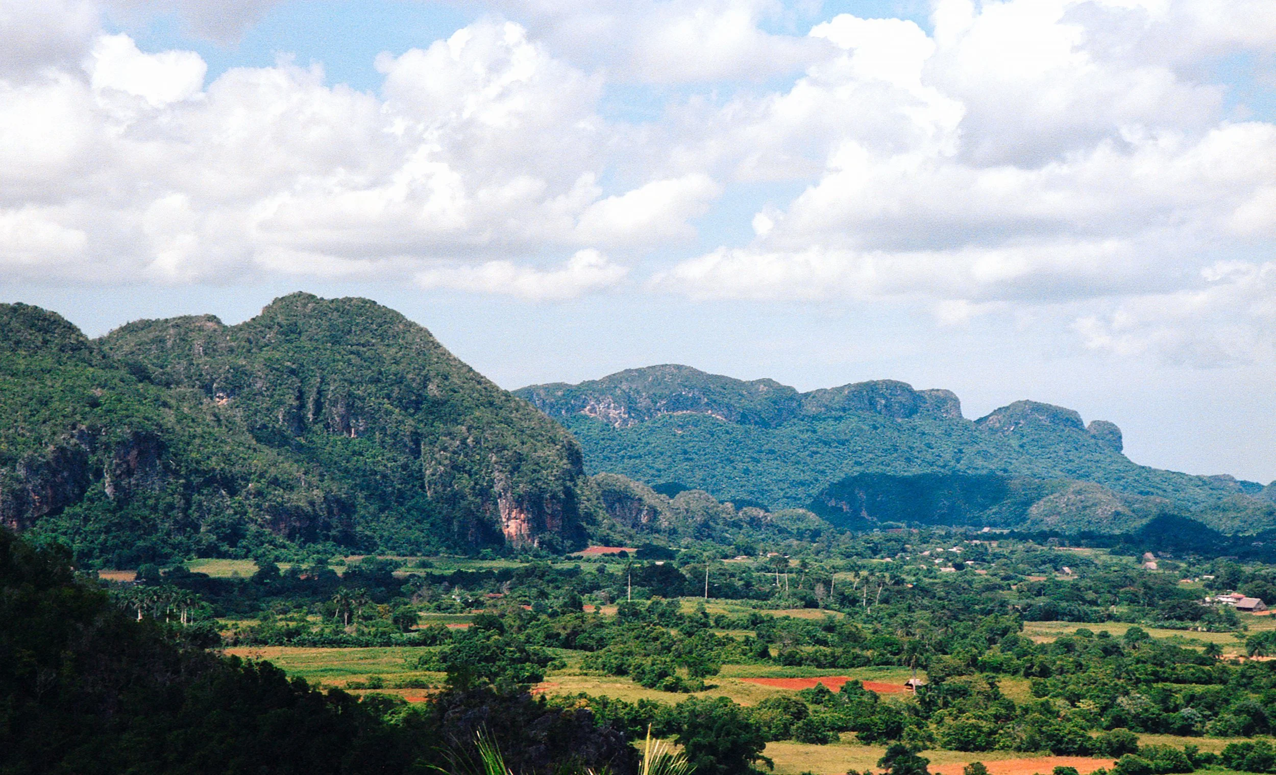Scenic landscape with lush green mountains, farmland, and a partly cloudy sky.