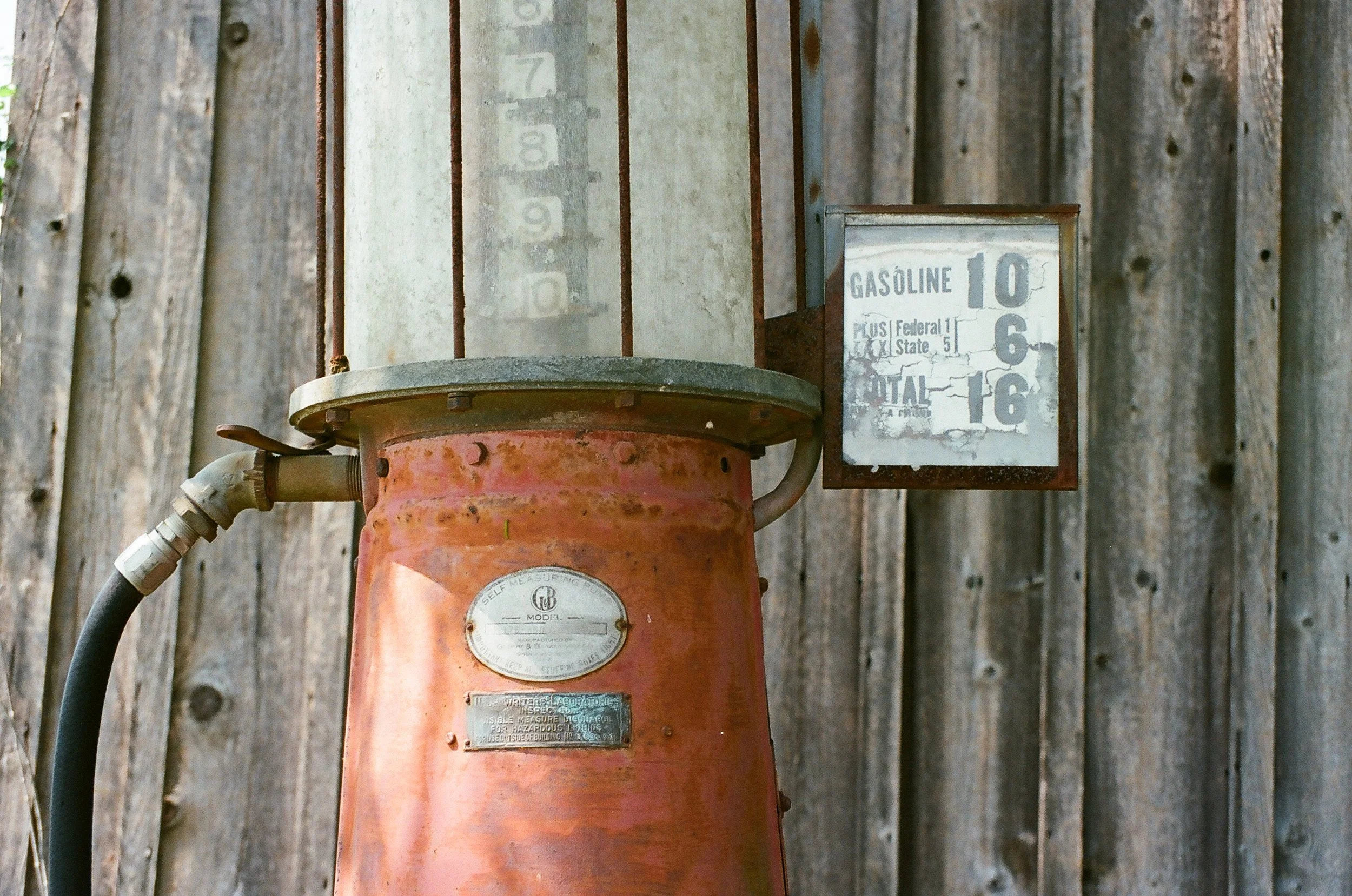 Old rusty gas pump with price sign and weathered wooden wall in the background.
