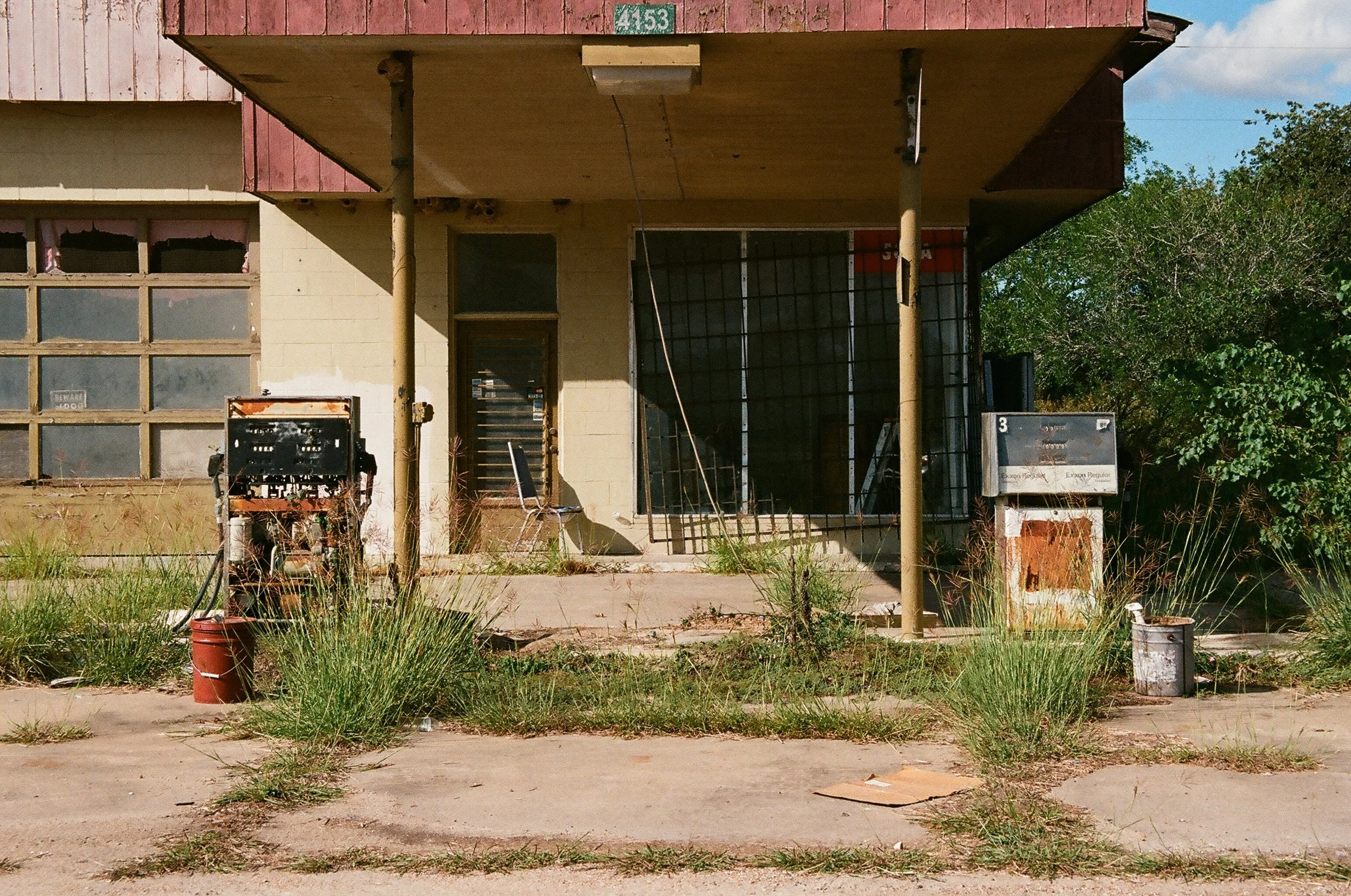 Abandoned building with broken windows, overgrown grass, and old USPS mailbox.