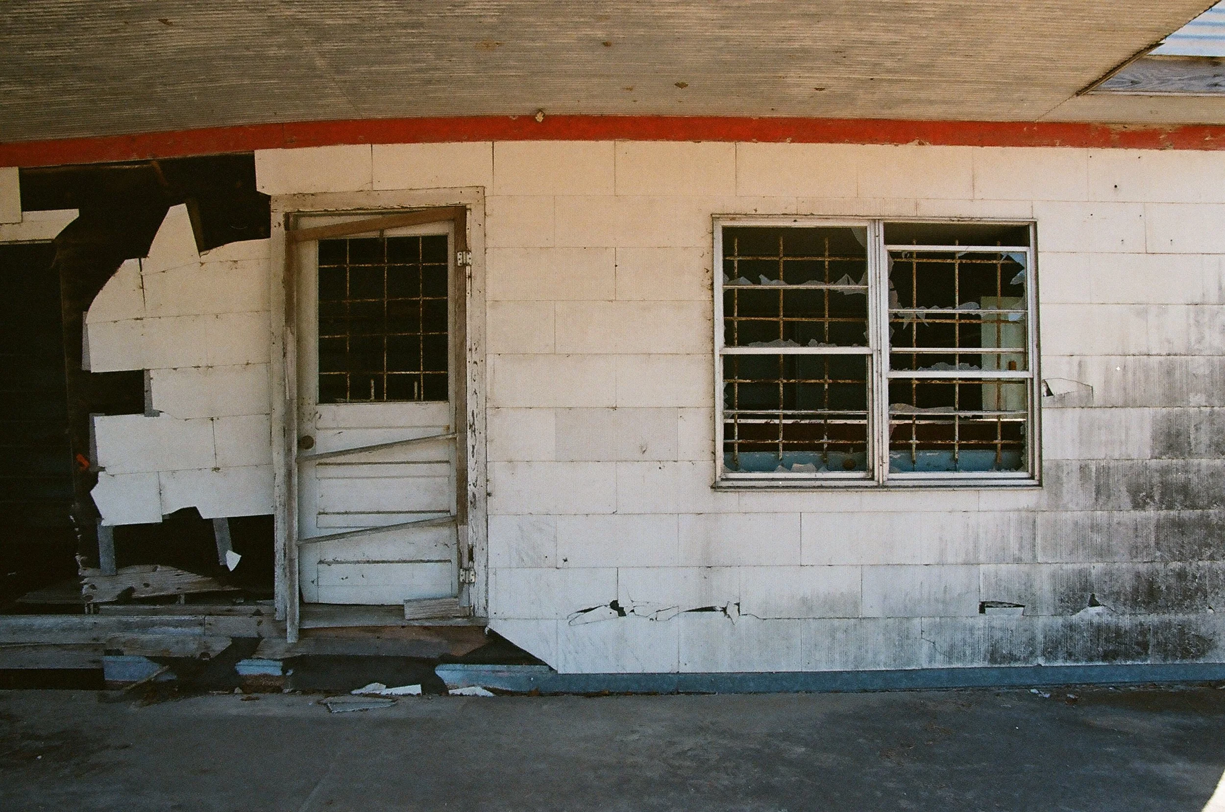 A worn, damaged house with peeling white paint, broken window blinds, and a door with chipped paint, showing signs of neglect.