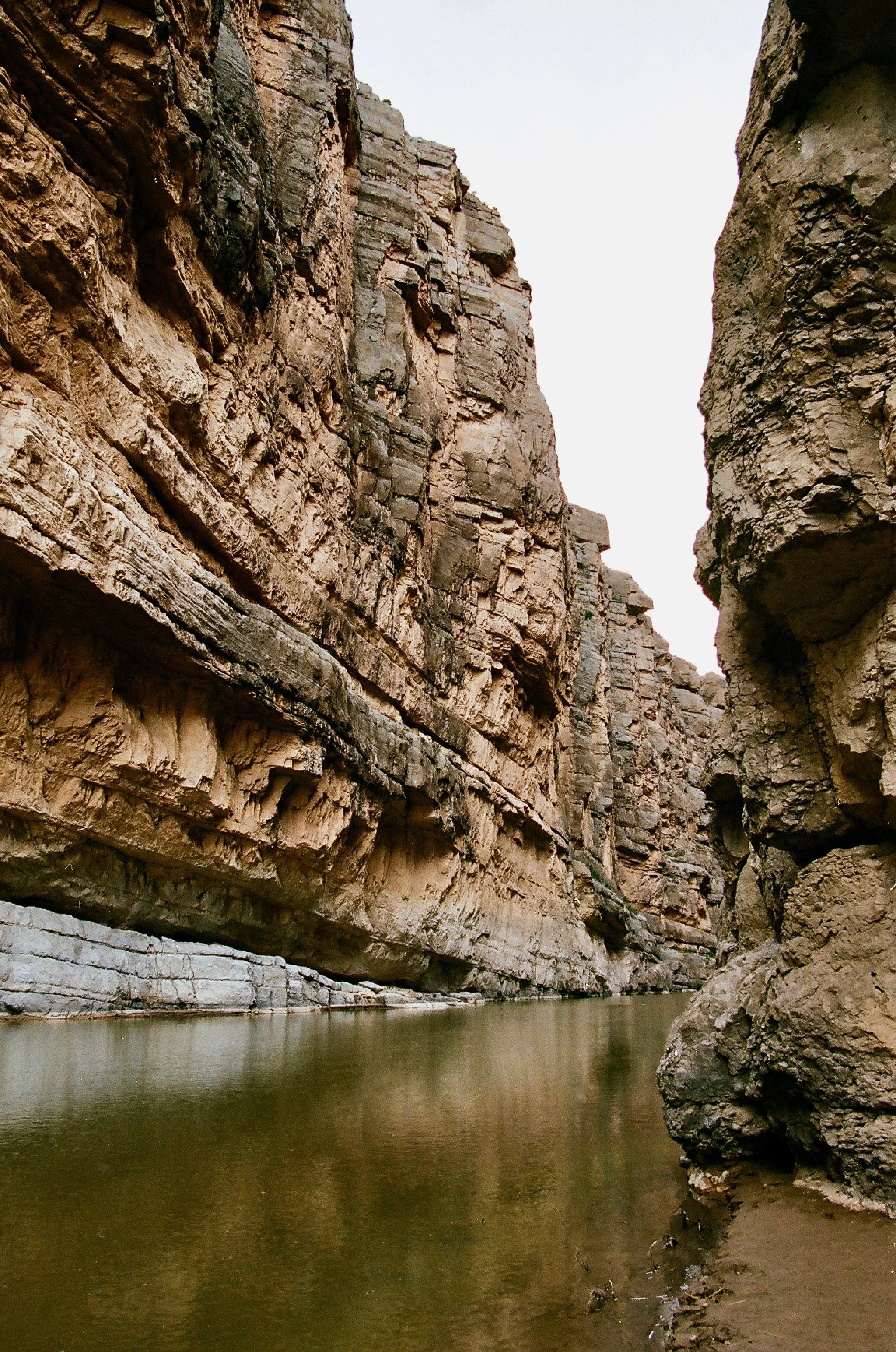 A narrow canyon with tall, rugged rock walls and a calm river flowing through the bottom.