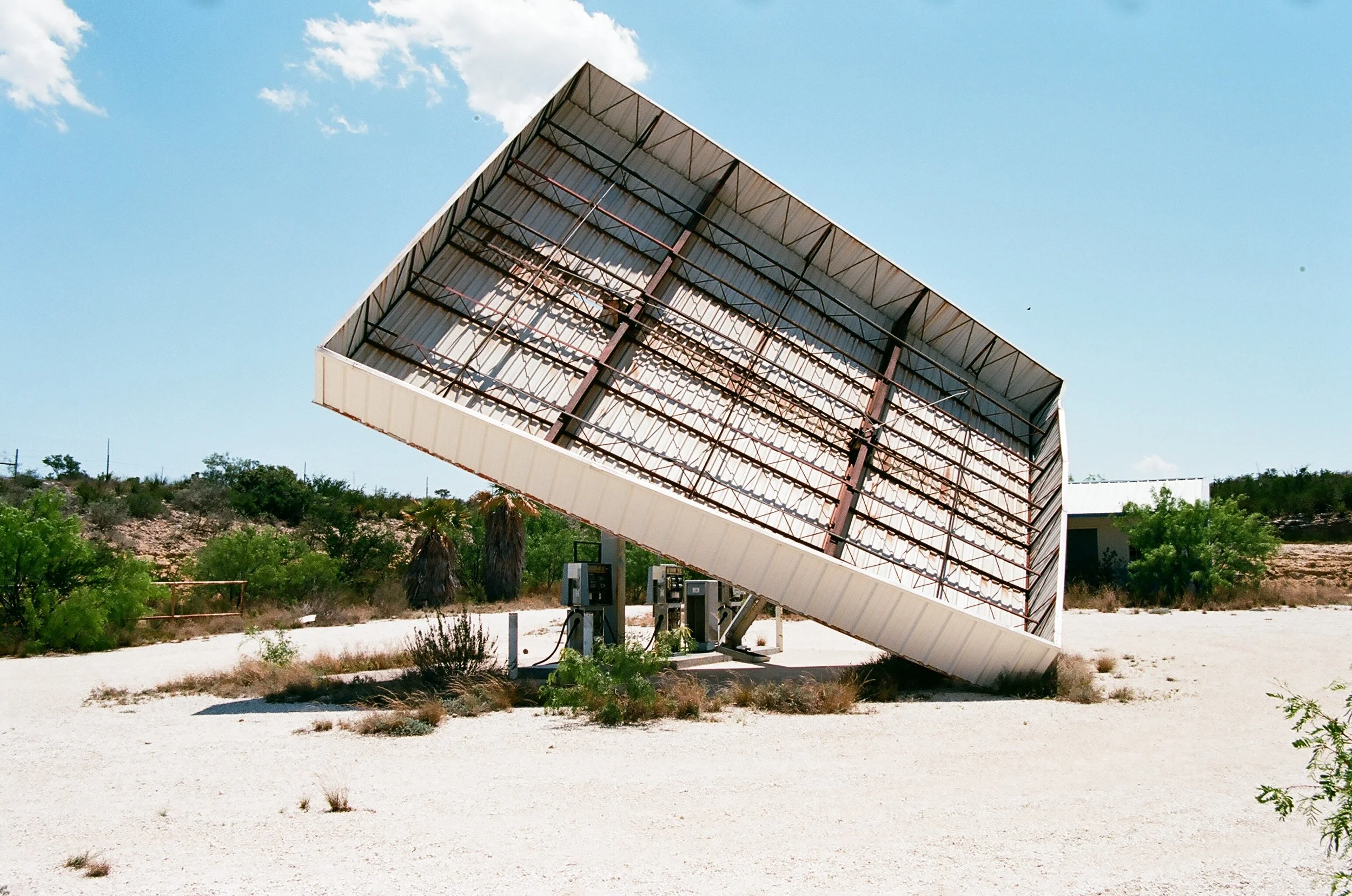 Large solar panel tilted at an angle in a desert landscape with shrubs and clear blue sky.