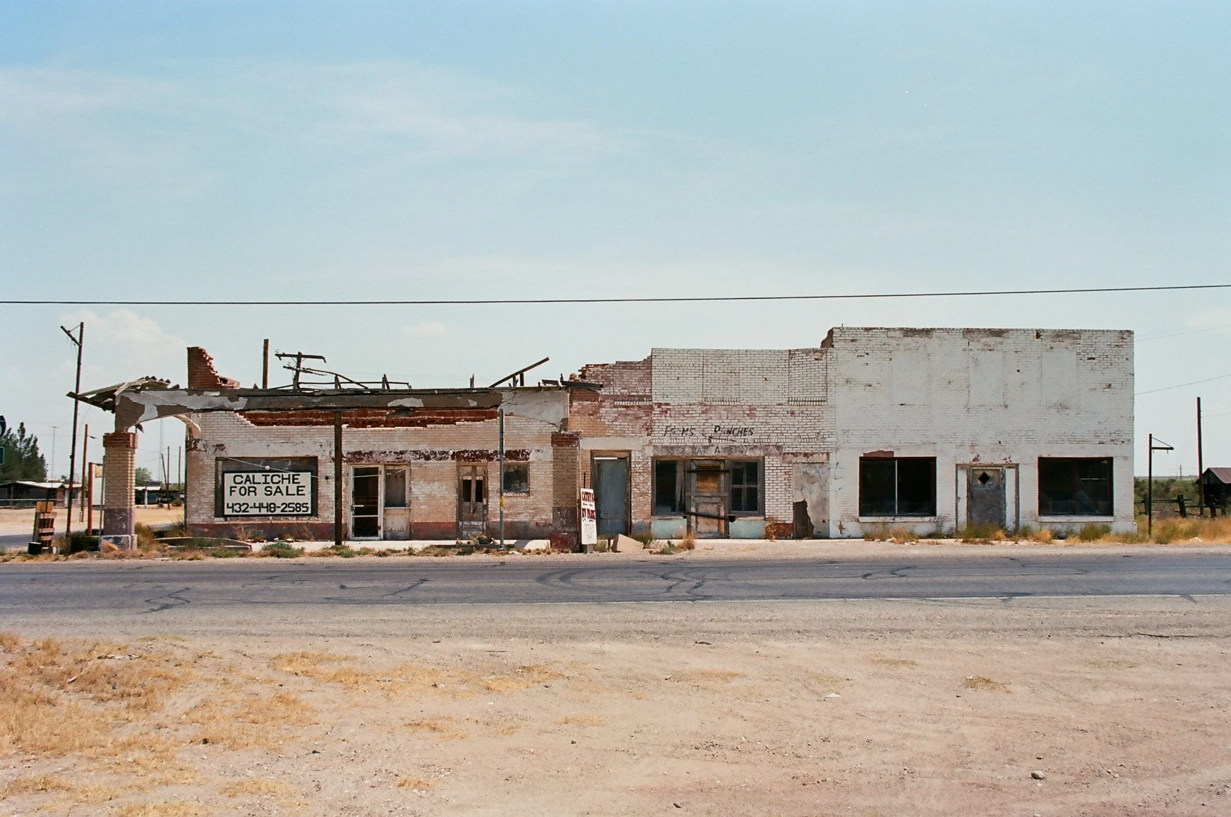 An abandoned, dilapidated building on the side of a rural road with a 