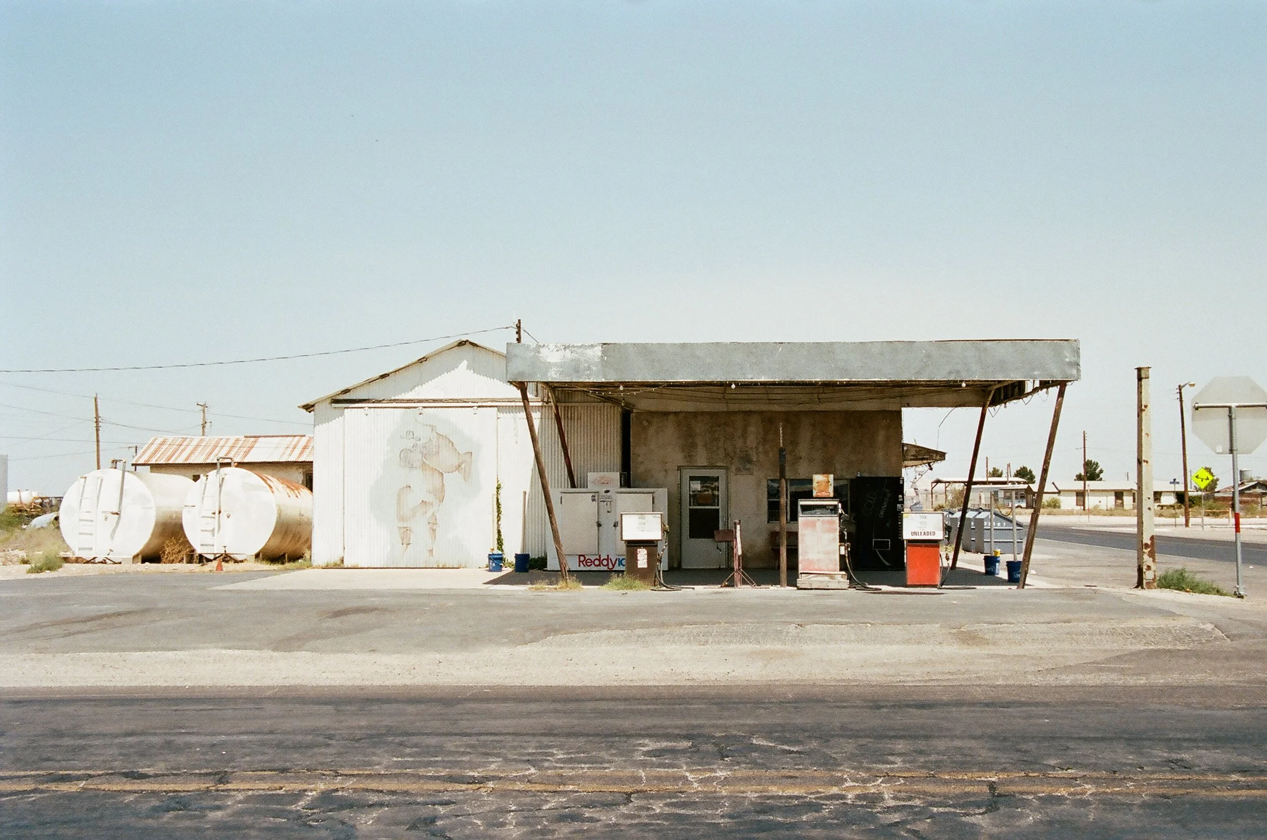 Old, weathered gas station with rusty tanks and abandoned look in a rural area, under a clear sky.