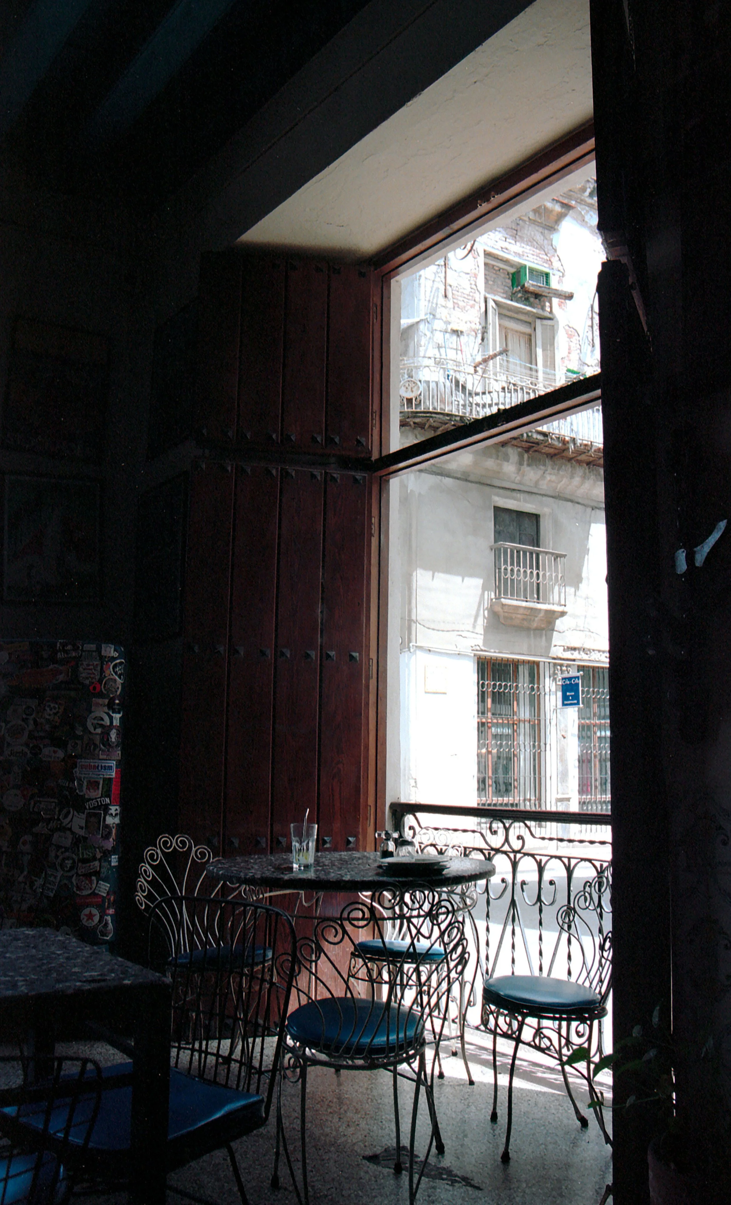 Interior of a cafe or restaurant with wrought iron chairs and a round table, with a large window showing buildings outside.