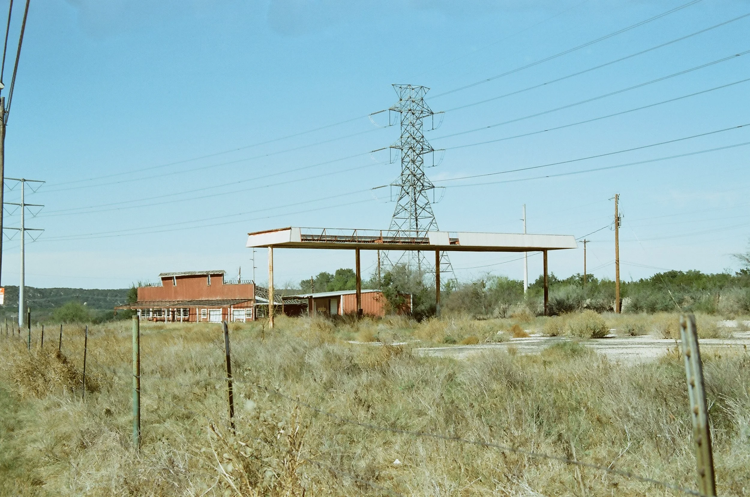 Desert landscape with an abandoned building, a metal canopy, and power lines in the background.