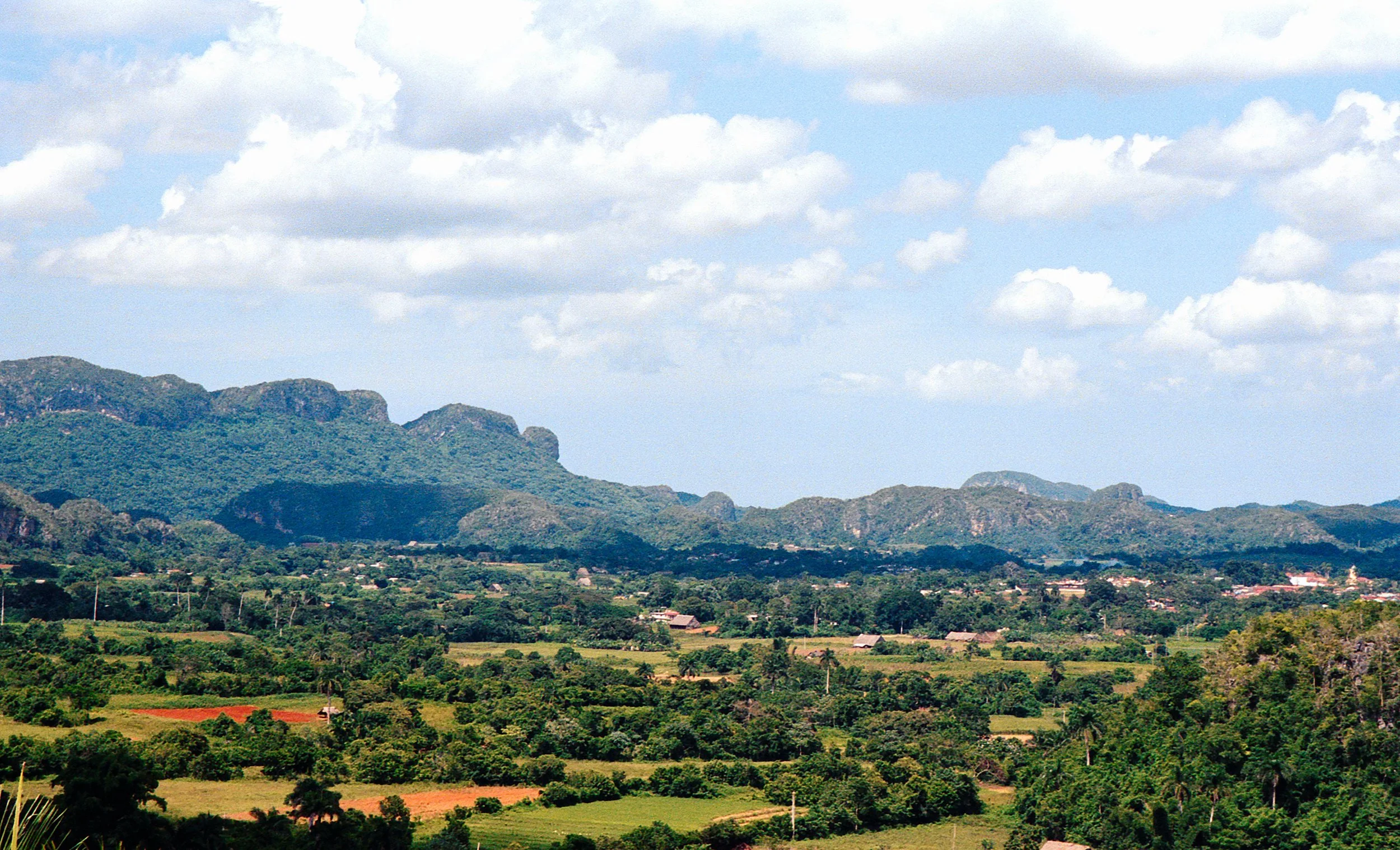 Scenic view of rolling green hills, distant mountains, and a partly cloudy sky.