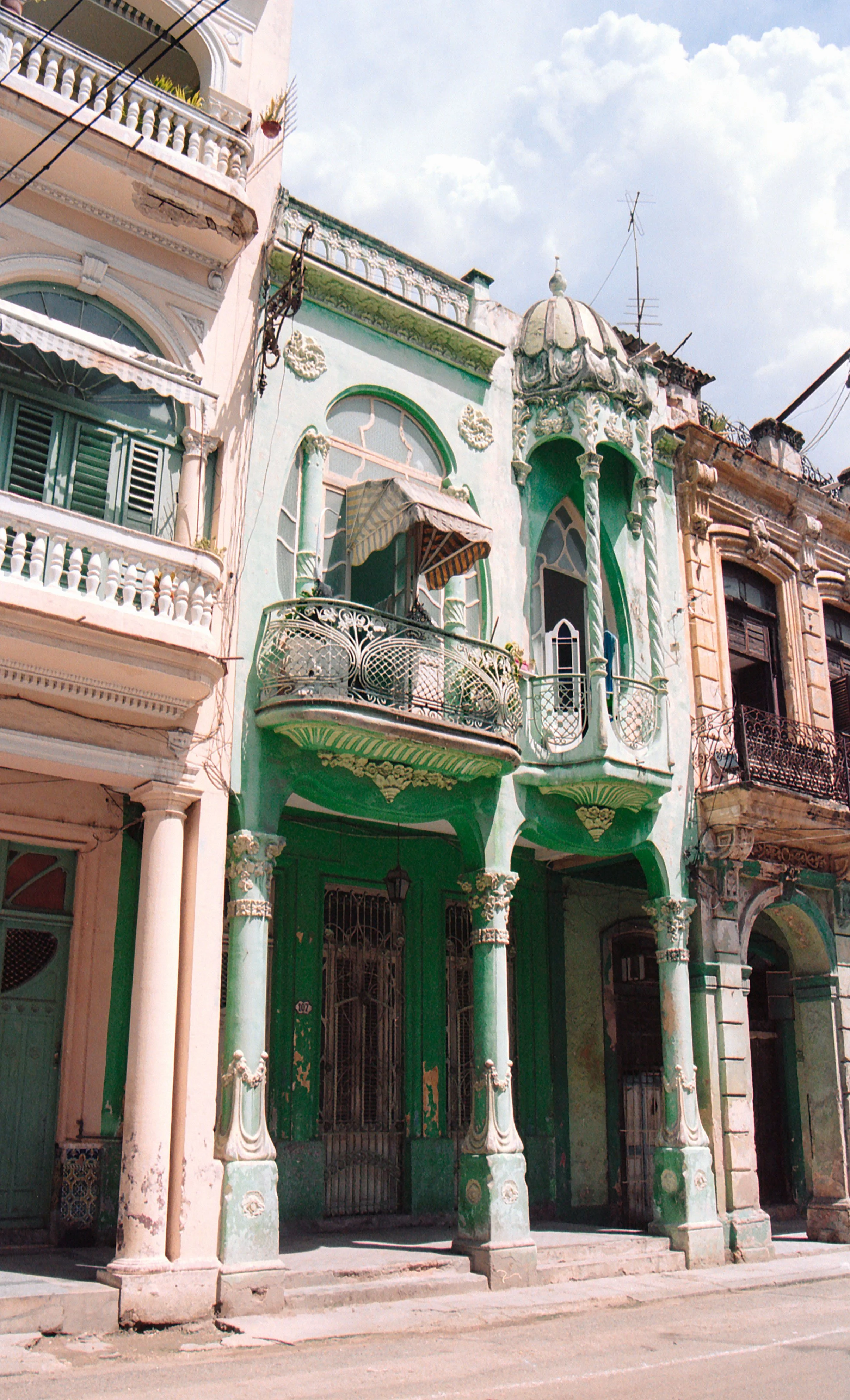 Colorful, ornate buildings with balconies and decorative architecture on a street under a partly cloudy sky.