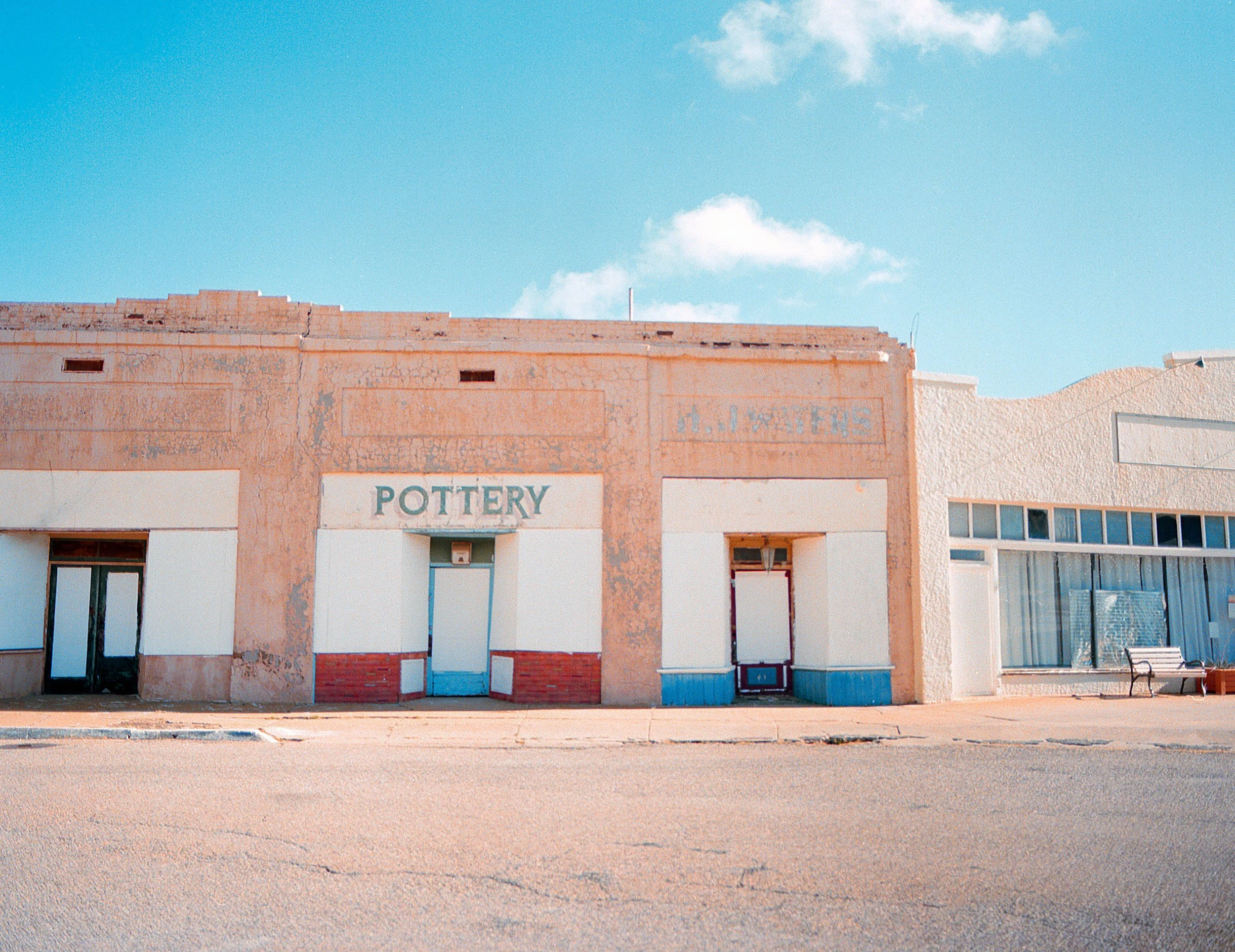 Old building with a sign that says 'POTTERY' on it, in a small town under a blue sky with a few clouds.