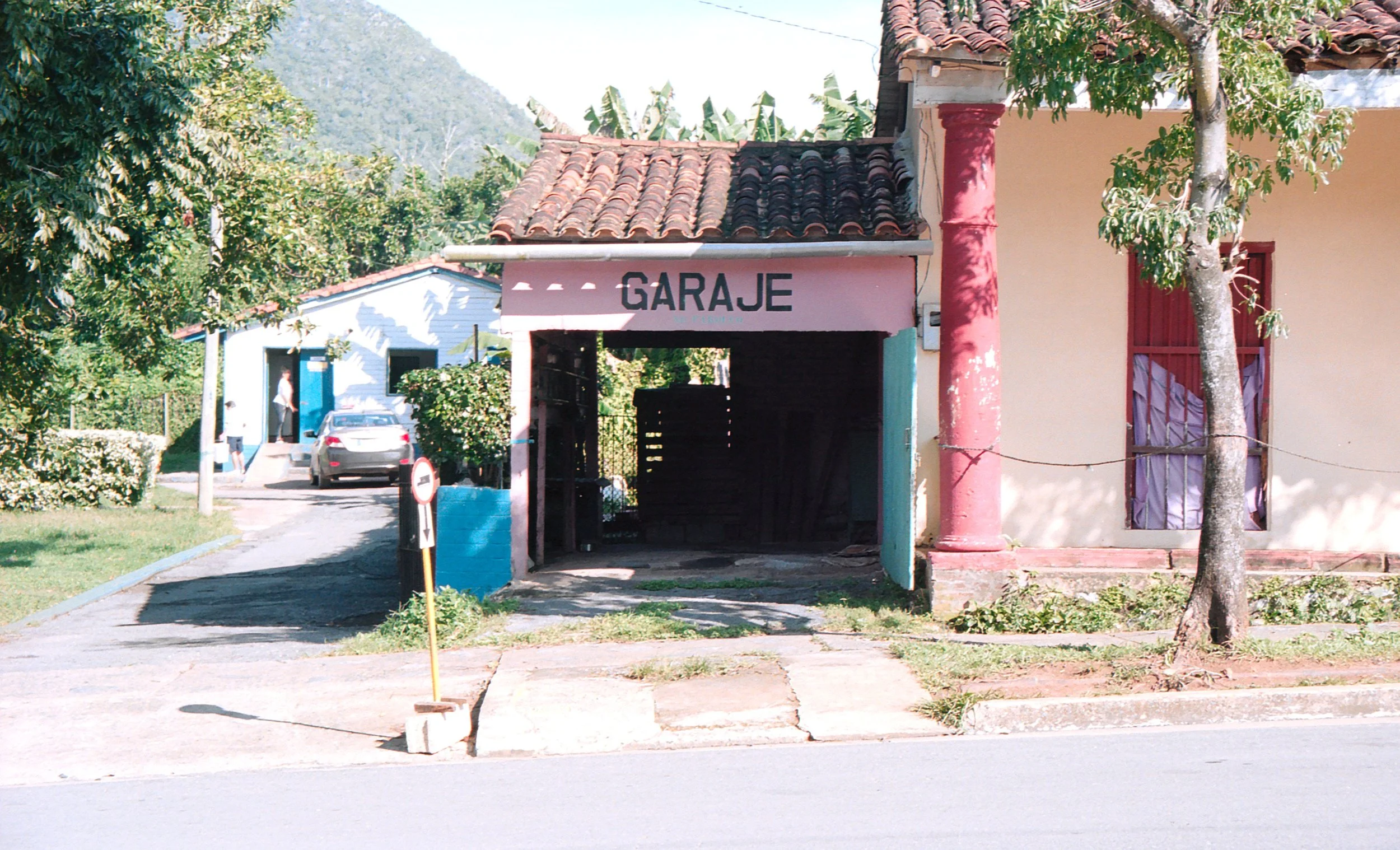 A building with a sign that says 'GARAJE', indicating a garage, located on a street with trees and parked cars in a residential area.