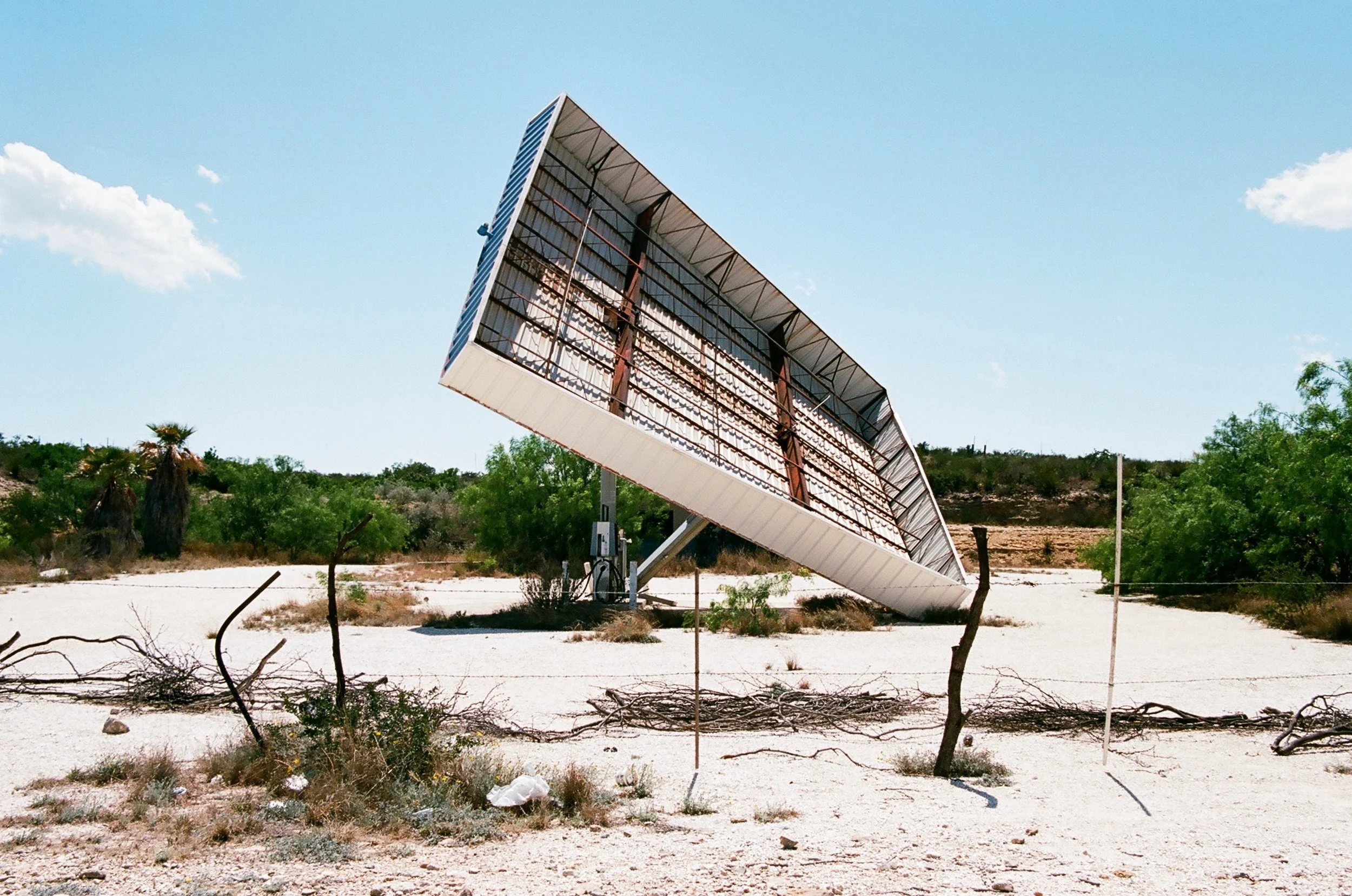 A solar panel tilted toward the sky in a desert landscape with sparse vegetation and blue sky.
