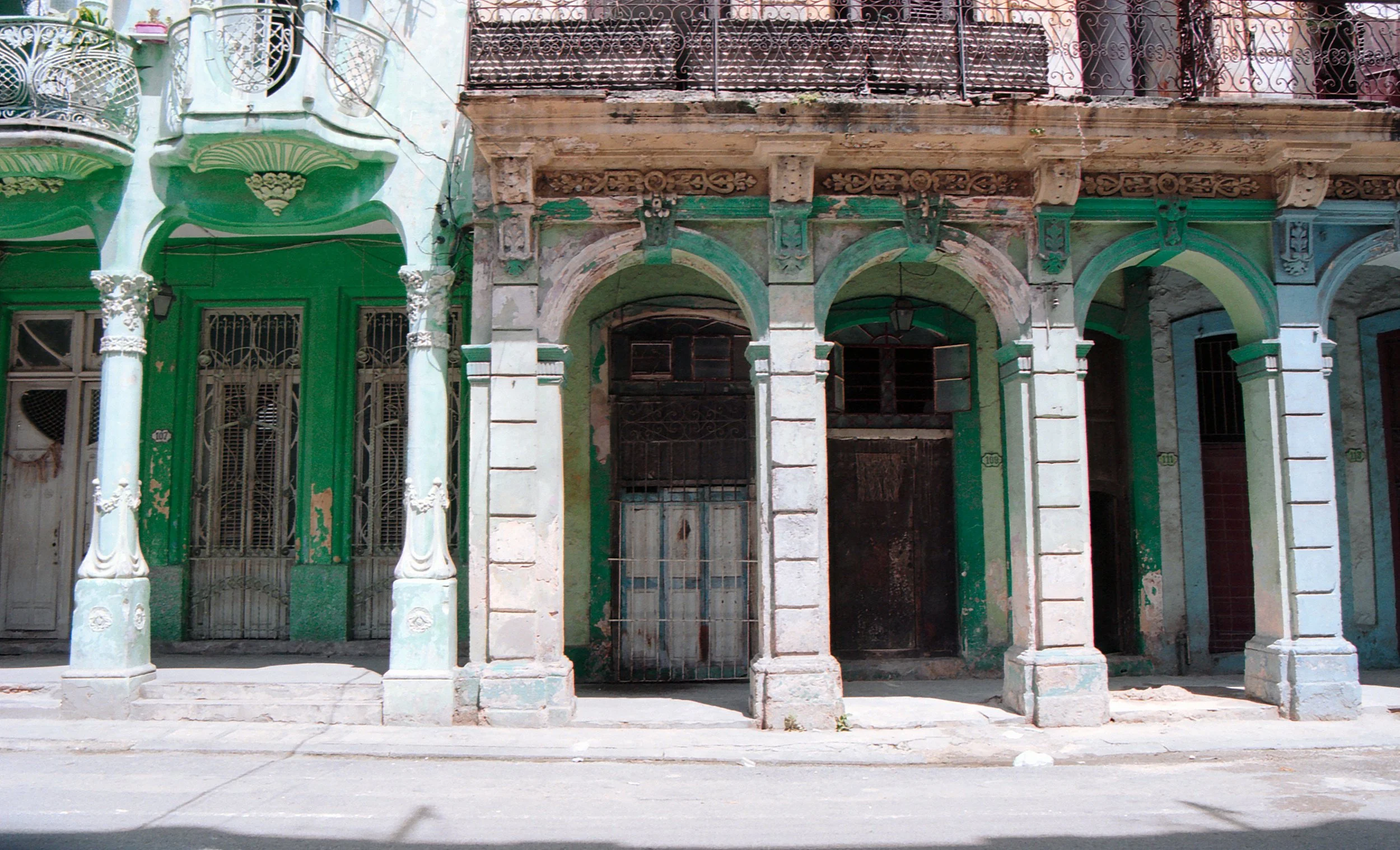 Old, weathered building with arched entrance, peeling paint, and intricate wrought iron balconies, typical of colonial architecture.