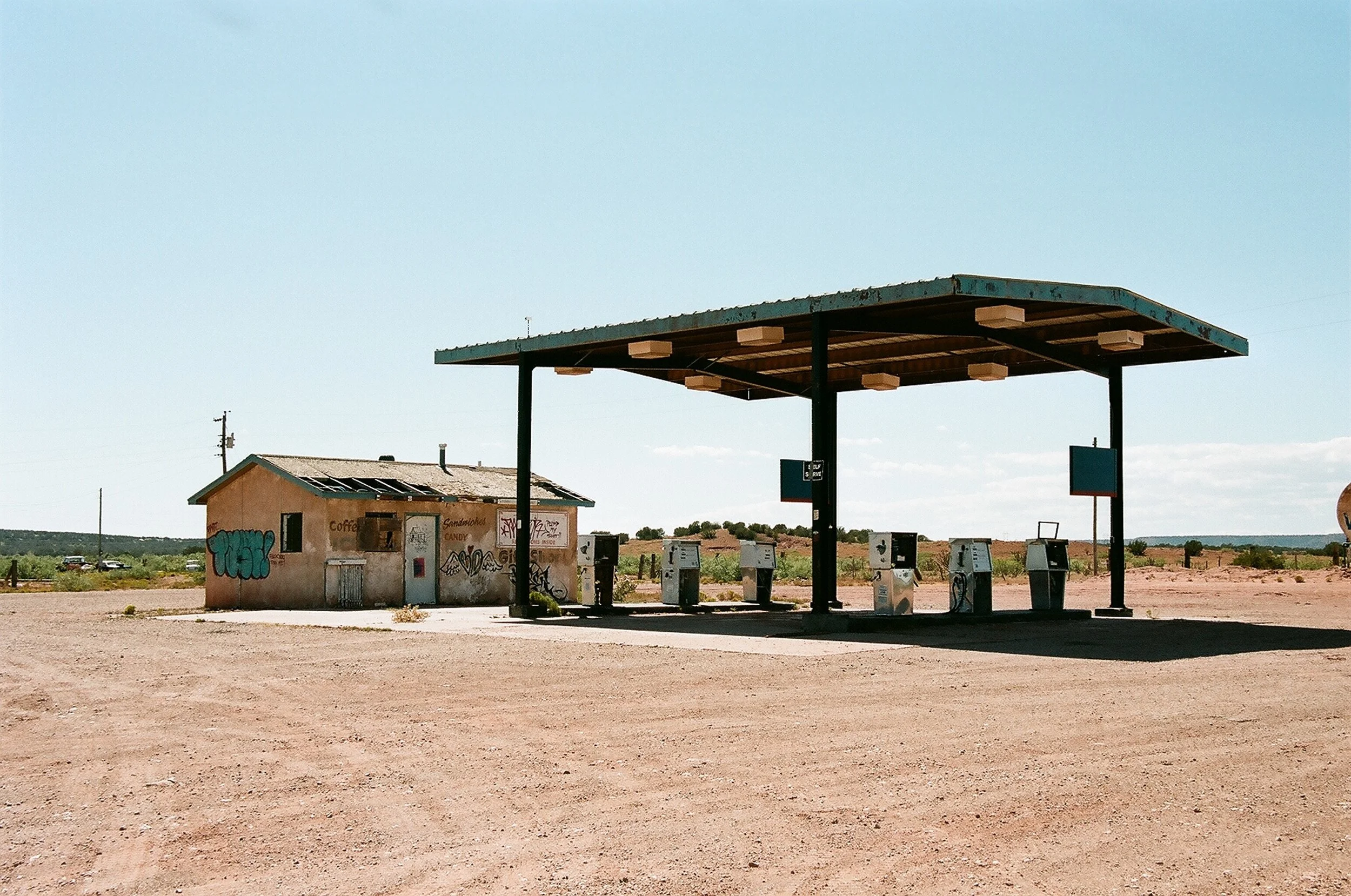 Empty rural gas station and small building with graffiti in the desert under a clear blue sky.