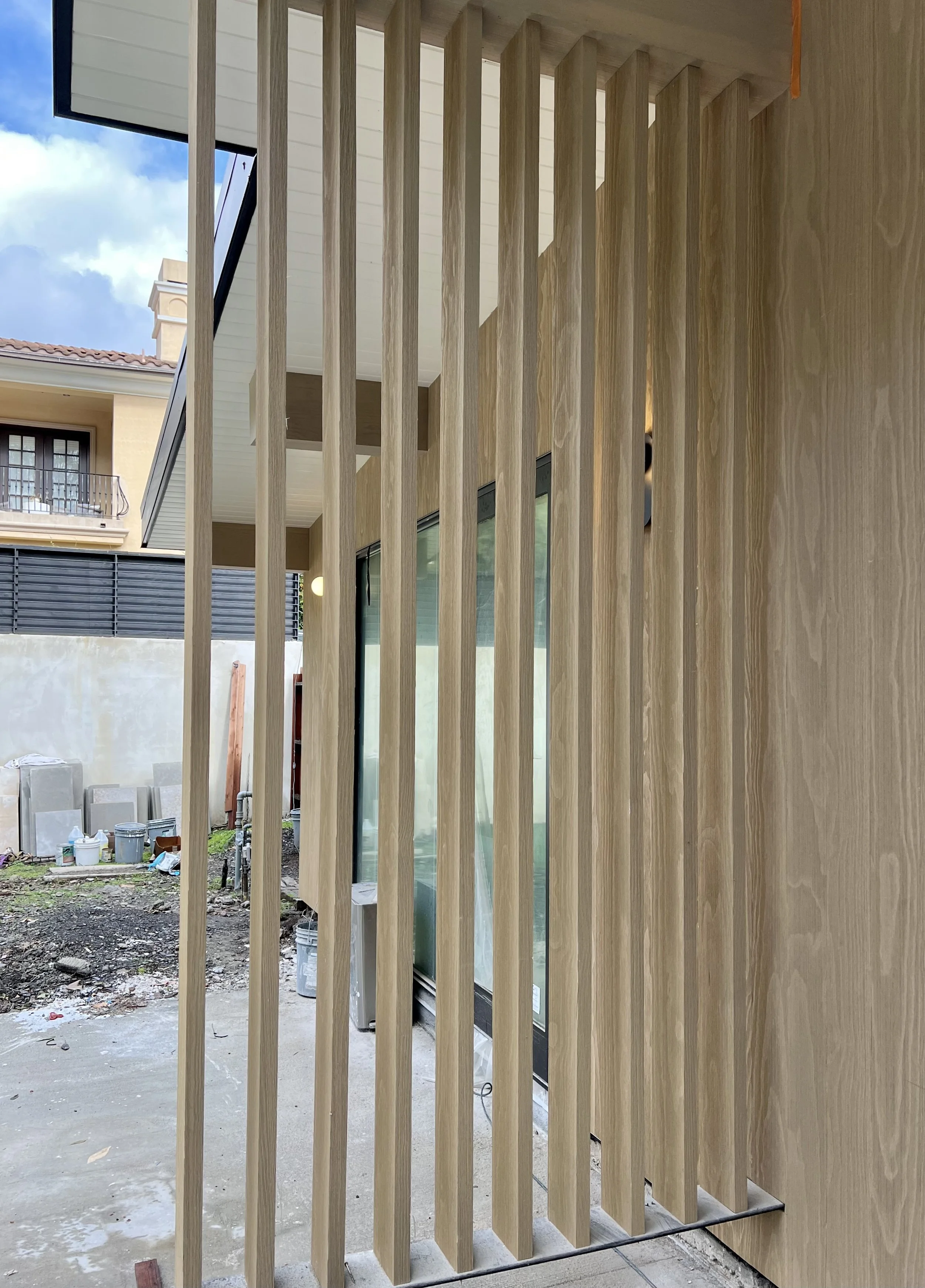 Wooden vertical slats exterior wall of a building under construction, with a glass sliding door and construction materials outside.