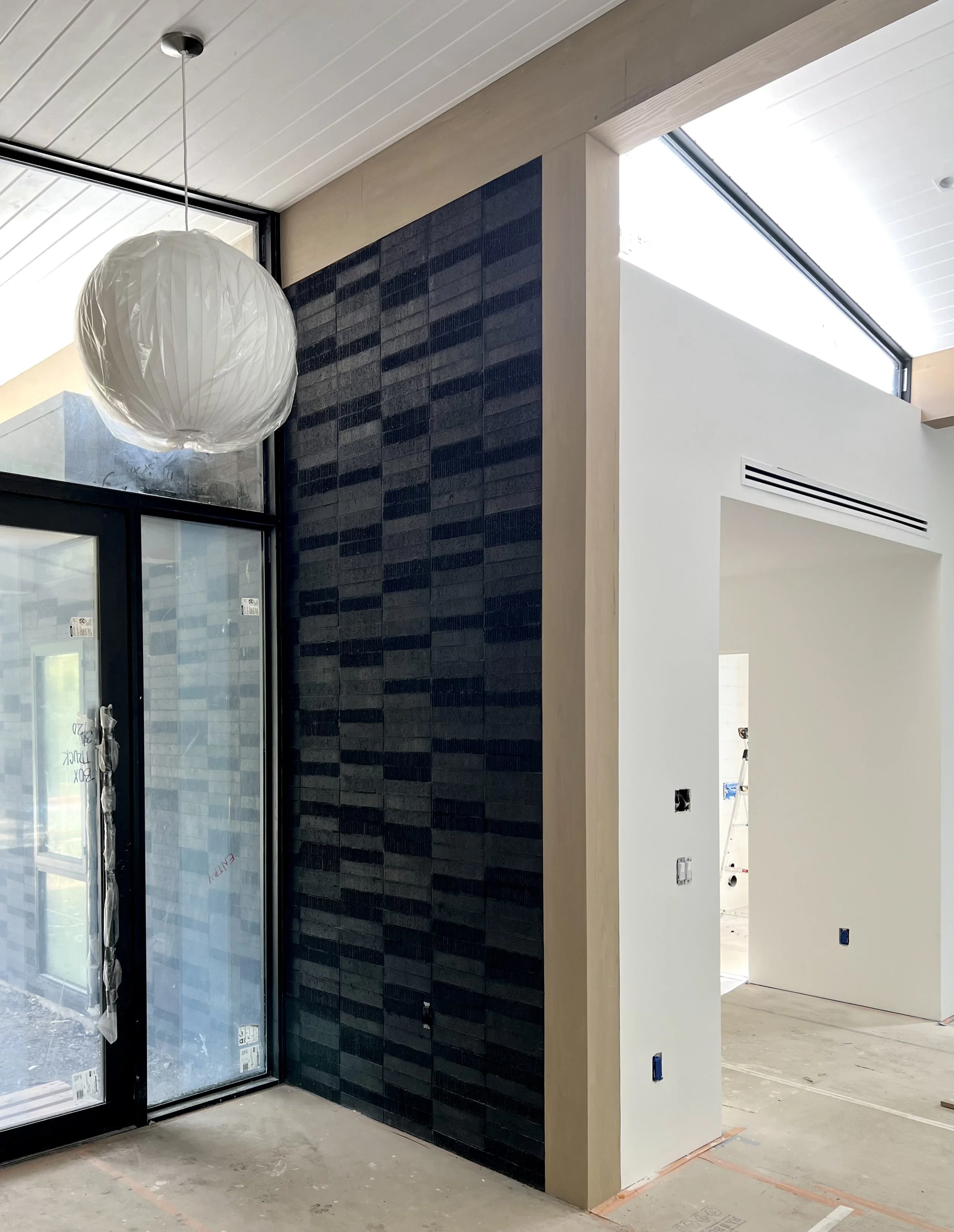 Interior of a house under construction with a black tile accent wall, a large window, and a paper lantern ceiling light.