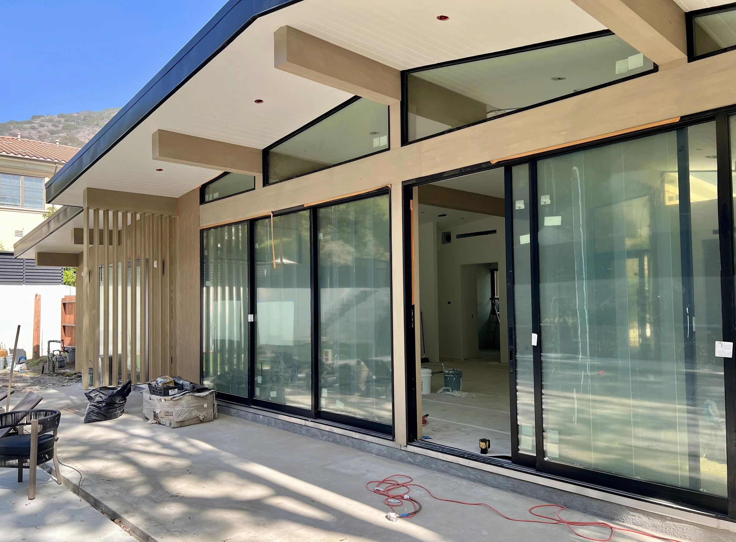 Under construction modern house with large glass sliding doors, wooden accents, and an open patio area.