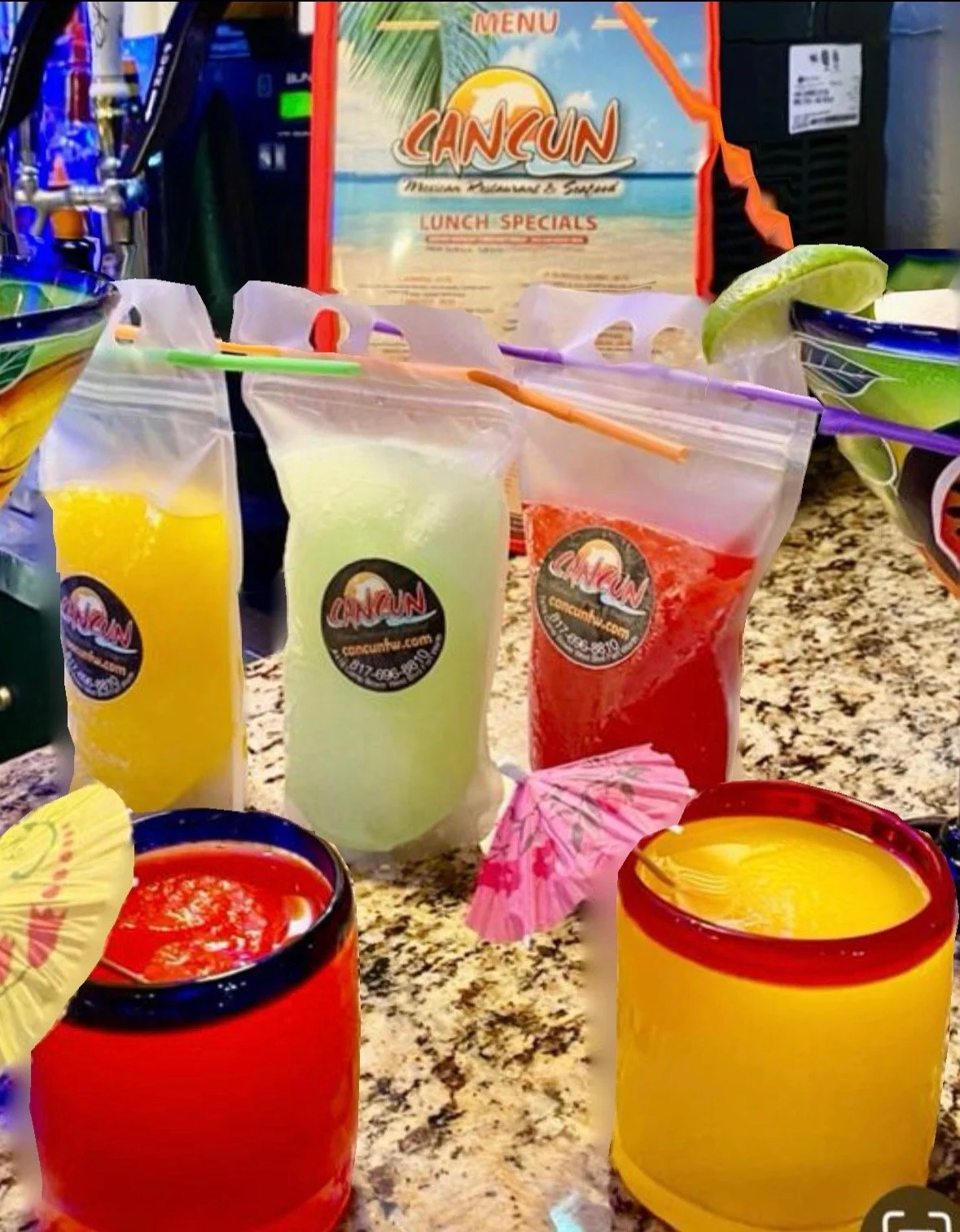 Assorted colorful frozen drinks in resealable plastic bags with cocktail umbrellas, on a granite counter, with a Cancun menu in the background.
