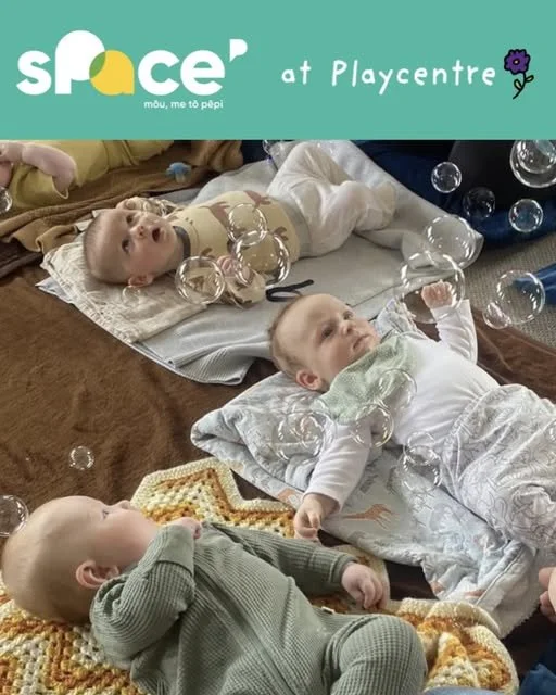Three babies laid on the ground watching bubbles at a Space playgroup