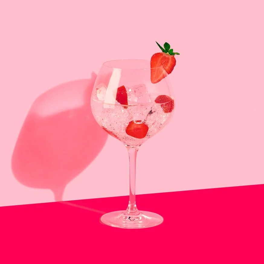 Gin och tonic med jordgubbar i ballongglas mot rosa bakgrund.