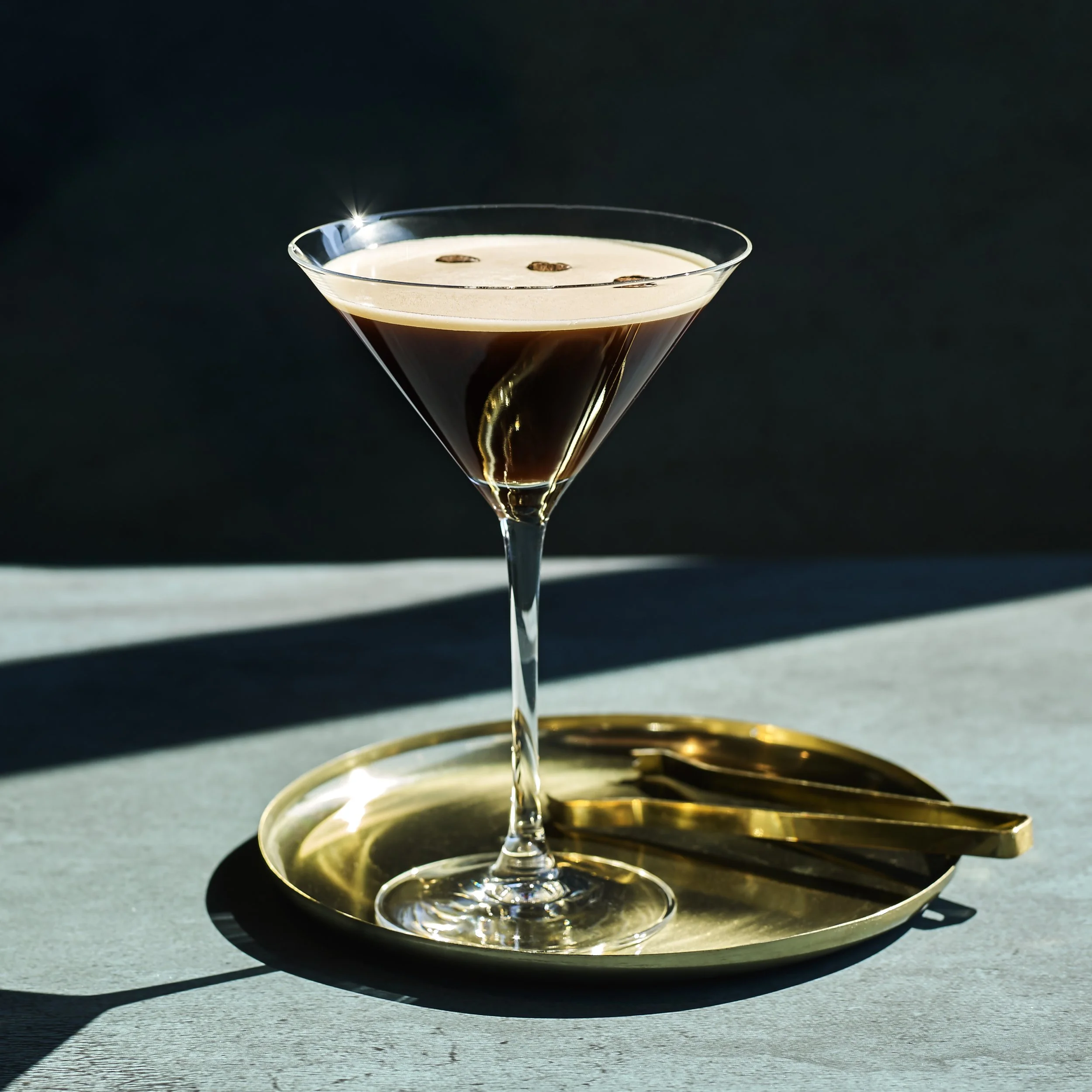 Espresso Martini cocktail i martiniglas med kaffebönor mot mörk bakgrund.