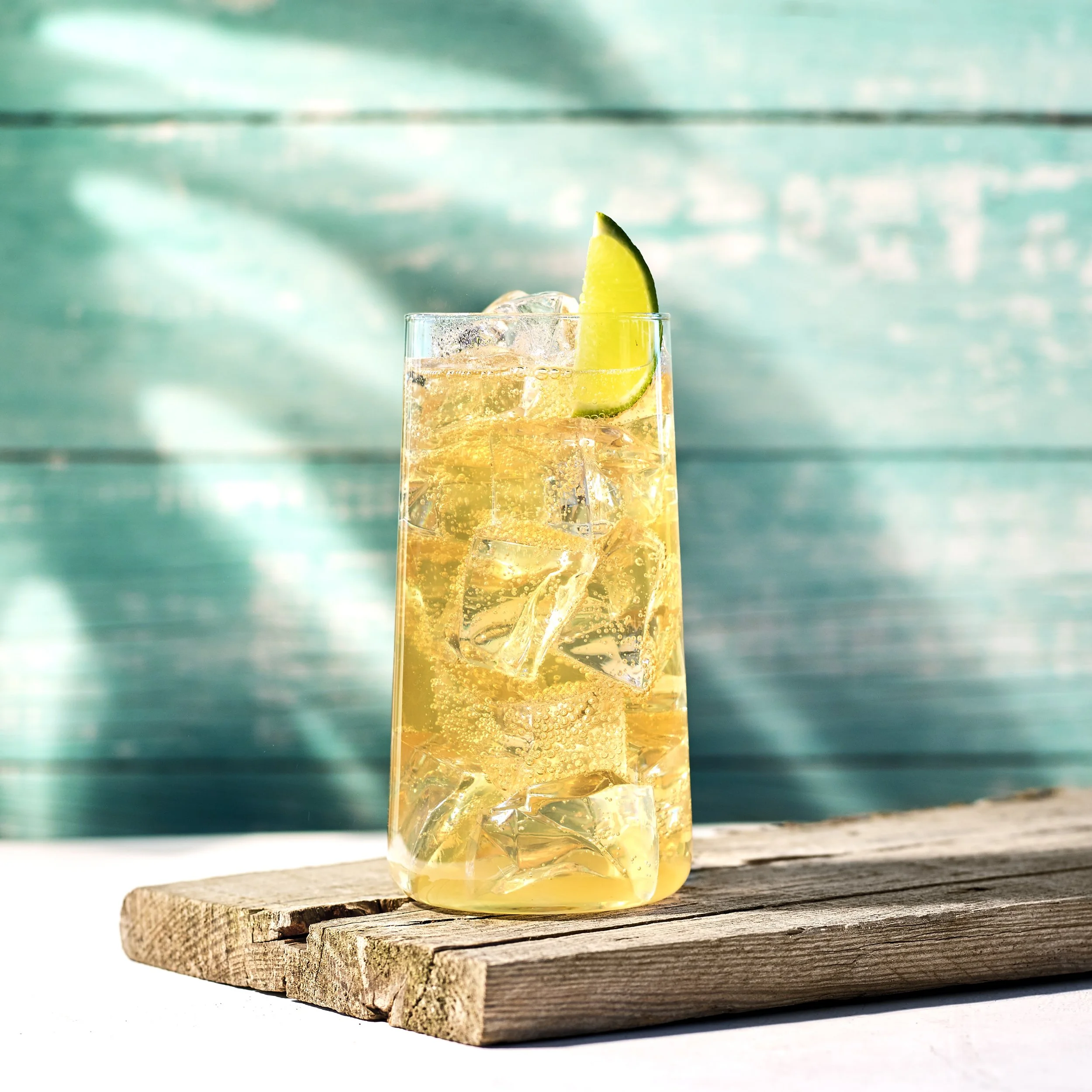 Dark ’n’ Stormy cocktail med lime och ginger beer i highballglas mot turkos träbakgrund.