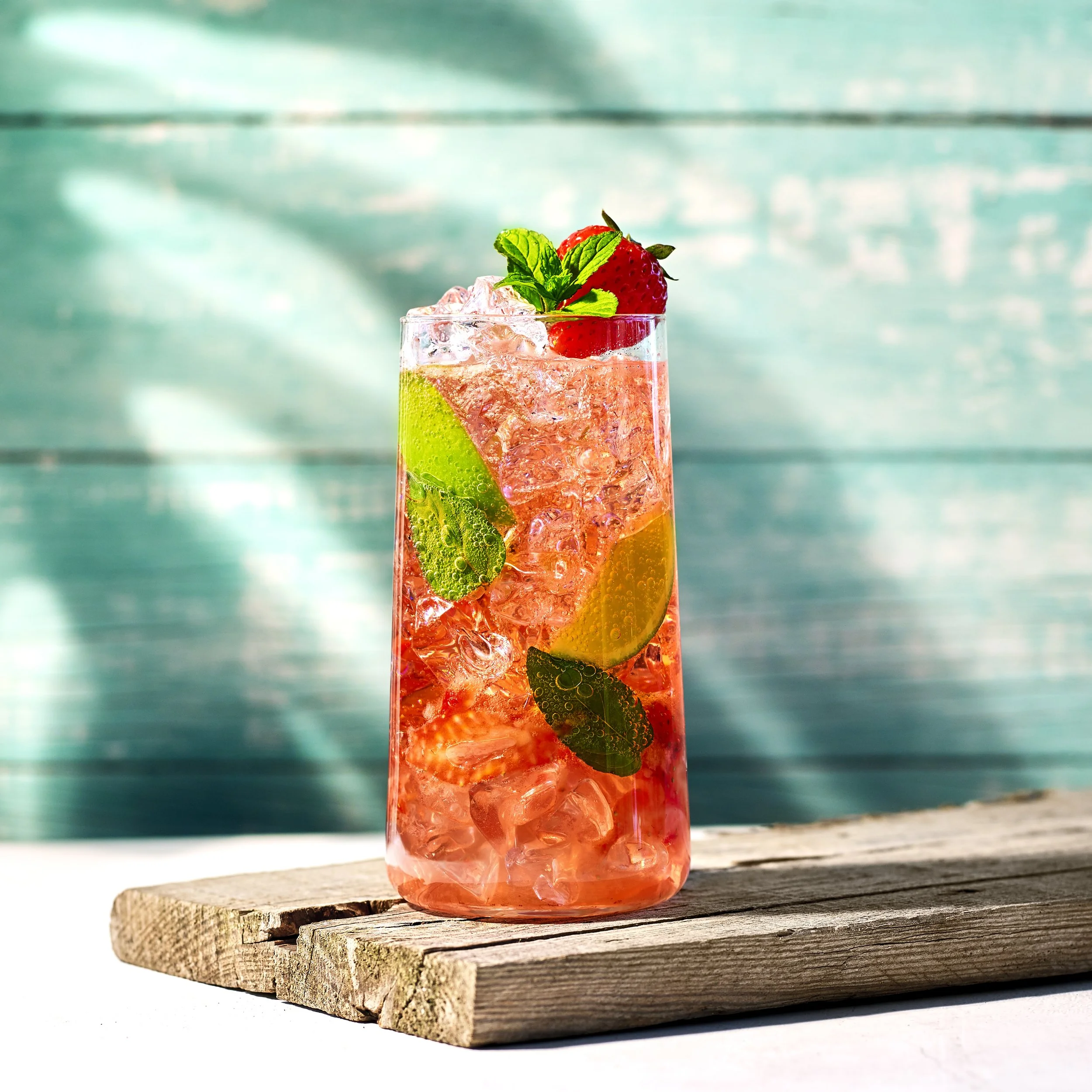 En Strawberry Mojito i ett högt glas med isbitar, dekorerad med skivor av jordgubbe och mynta.