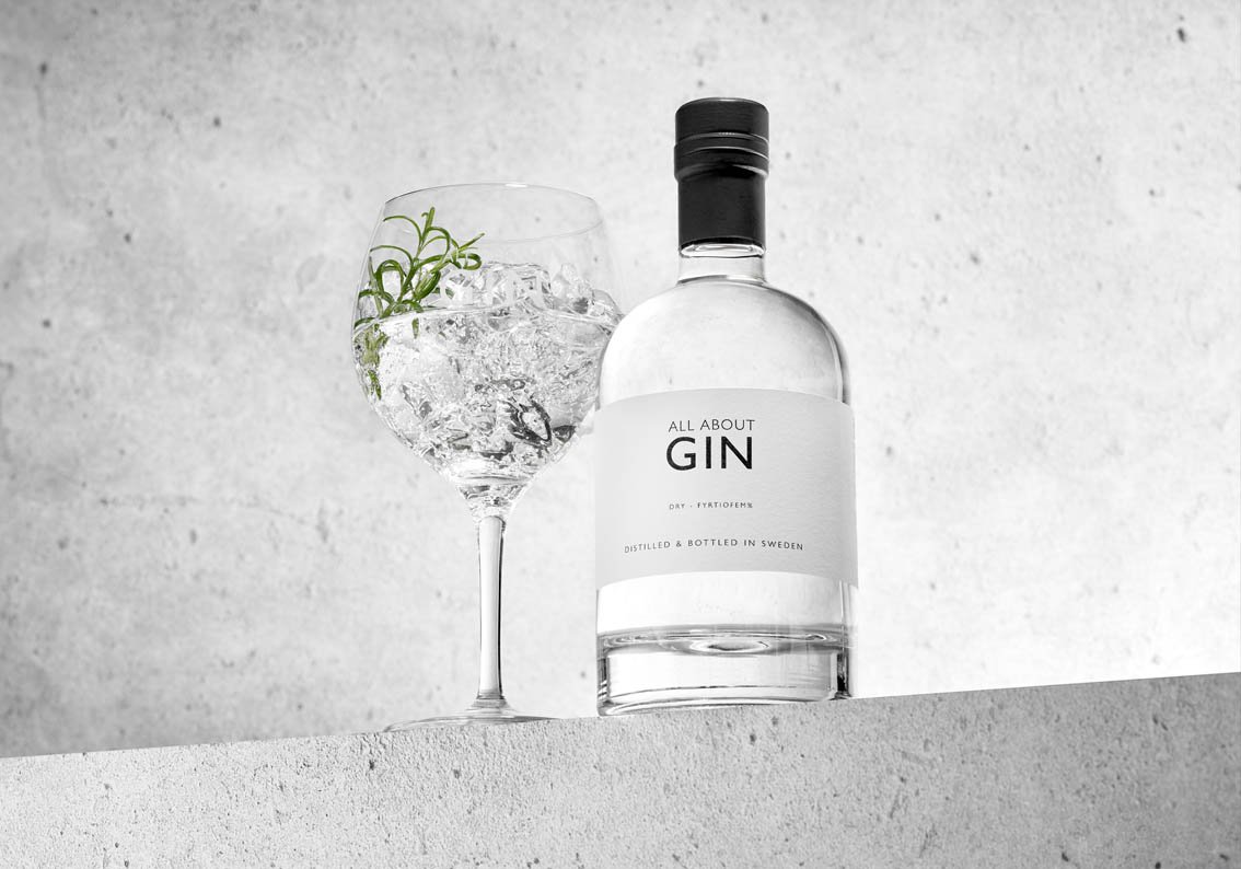 ll About Gin flaska tillsammans med ett glas gin och tonic med is och rosmarin