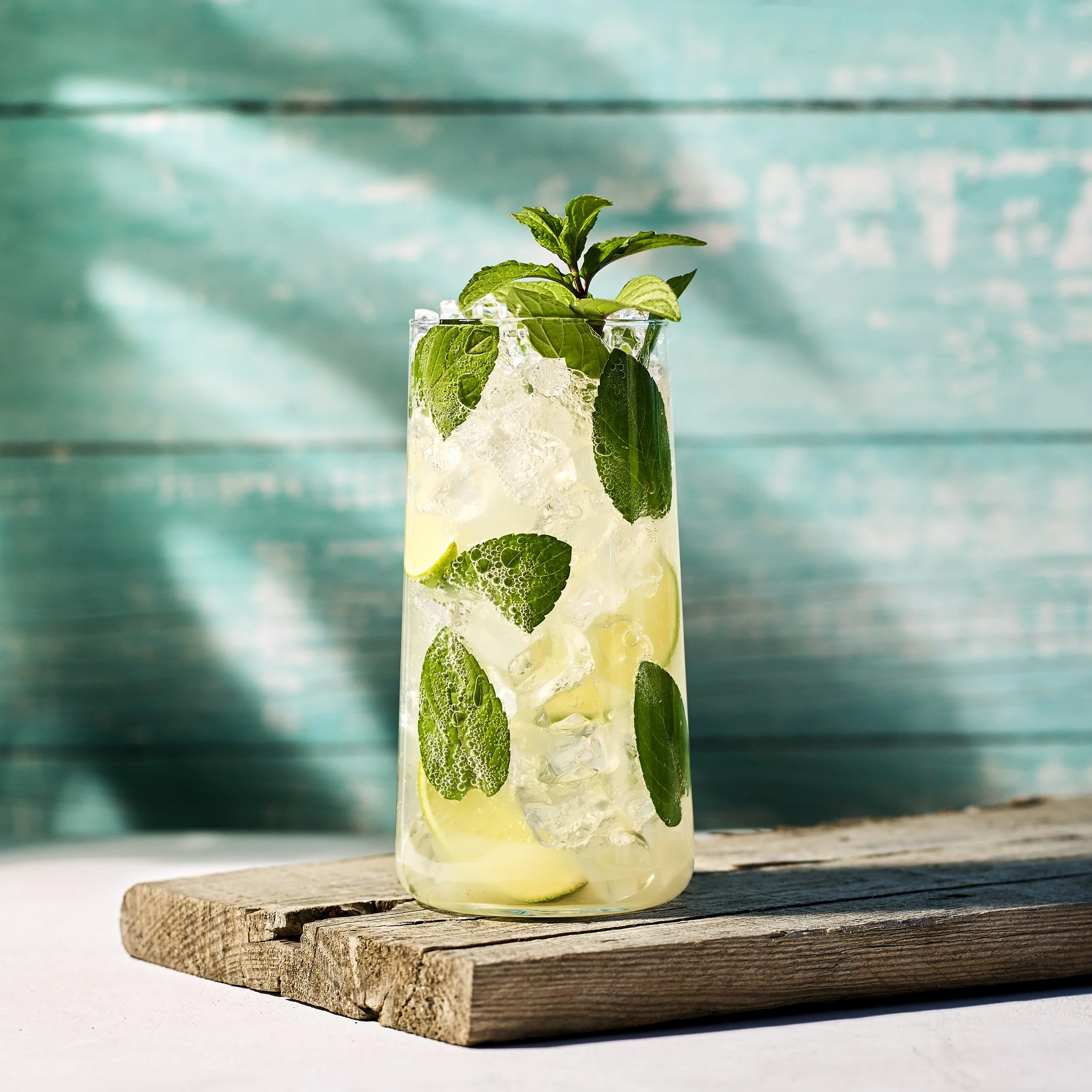 En Mojito i ett högt glas, fyllt med färska myntablad, limeklyftor och isbitar.