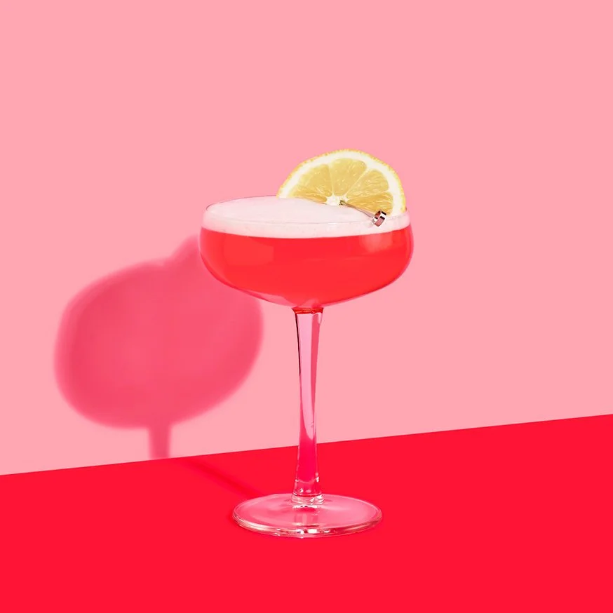 Vodka Sour med granatäpple i coupeglas mot rosa bakgrund.
