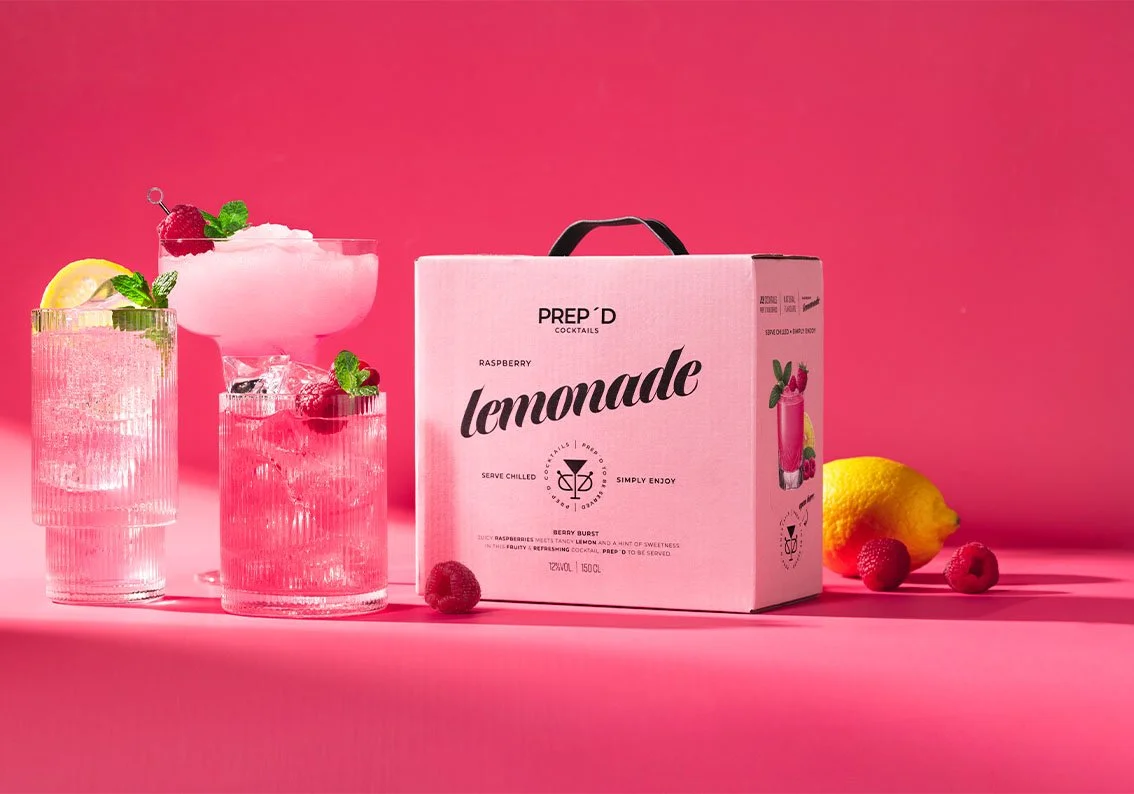 Prep´d Cocktails Raspberry Lemonade box med serverad rosa cocktail, hallon och citron på rosa bakgrund.