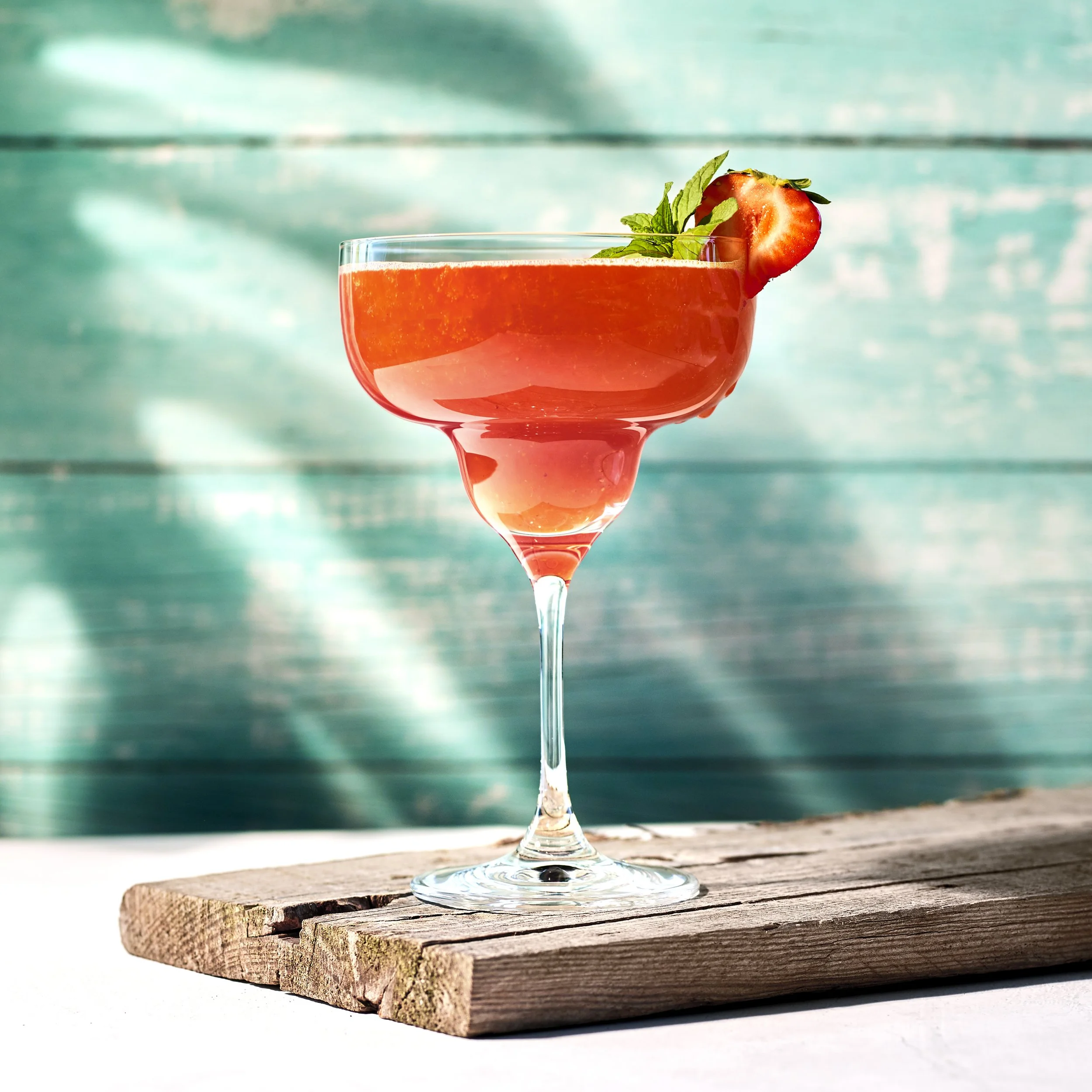 En Strawberry Daiquiri i ett stort, kupolformat cocktailglas. Drinken är garnerad med en skiva jordgubbe på kanten och ett litet blad mynta.