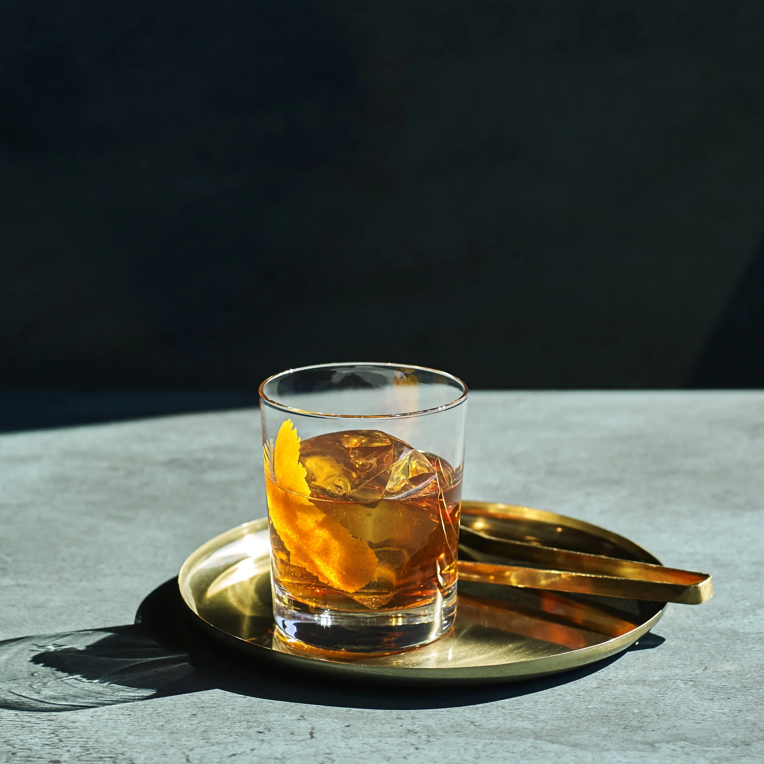 Old Fashioned cocktail med is och apelsintoner i rocksglas mot mörk bakgrund.