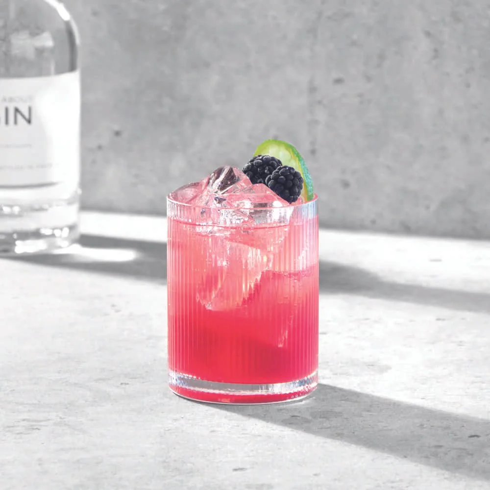 Bramble Breeze cocktail med björnbär och citrus mot grå bakgrund.